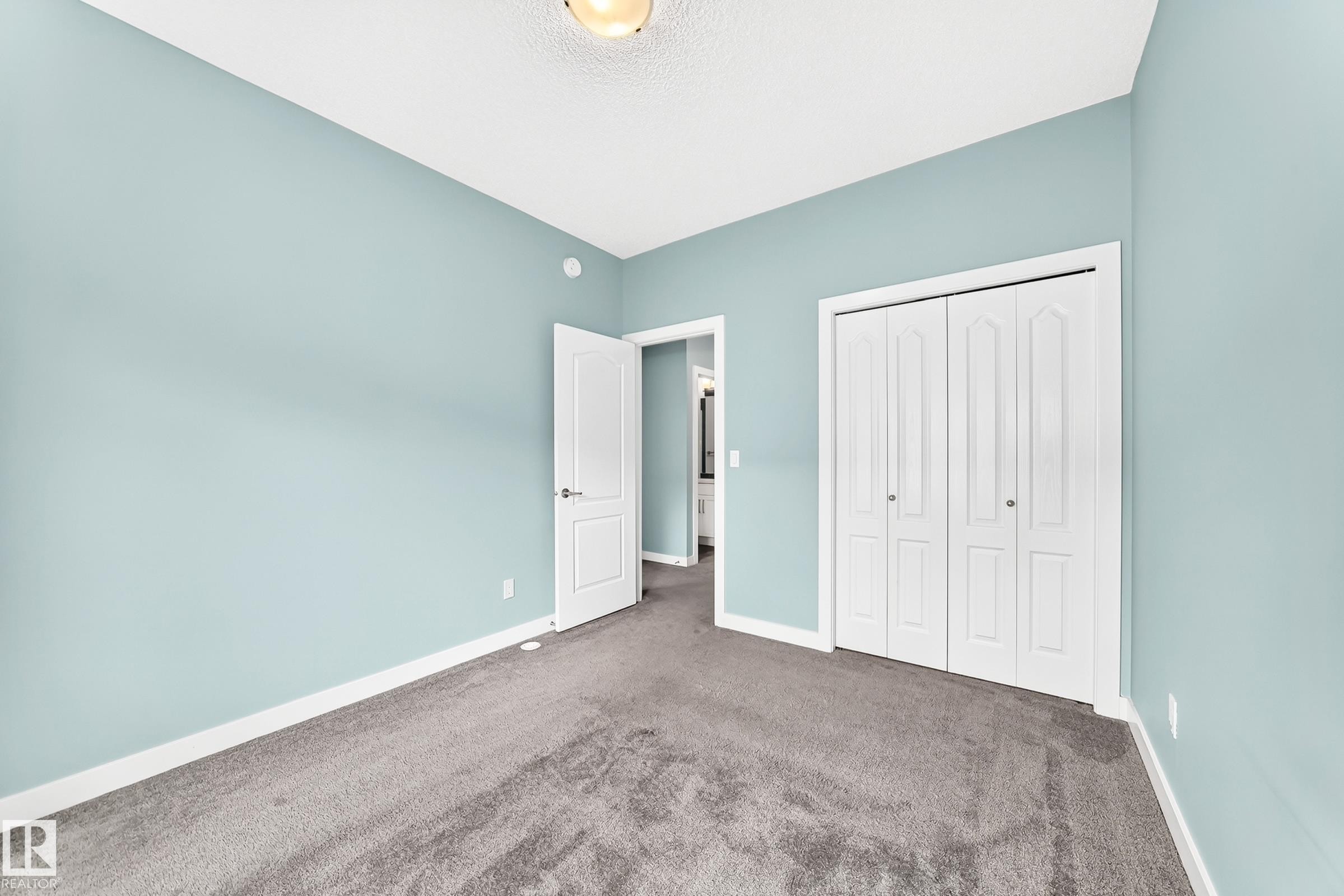 Textured carpeting, light blue wall paint, white trim, bifold closet doors, and a ceiling light fixture - #56 804 Welsh Dr Sw, Edmonton, AB