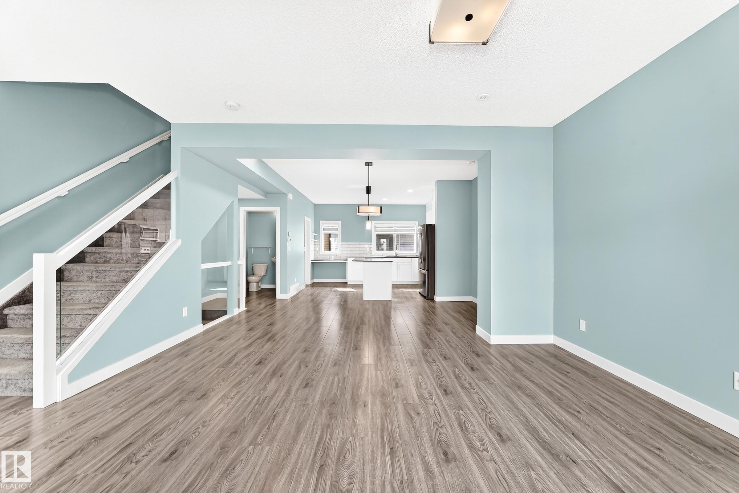 Wood-finish flooring throughout, with a carpeted staircase featuring a glass and white railing - #56 804 Welsh Dr Sw, Edmonton, AB
