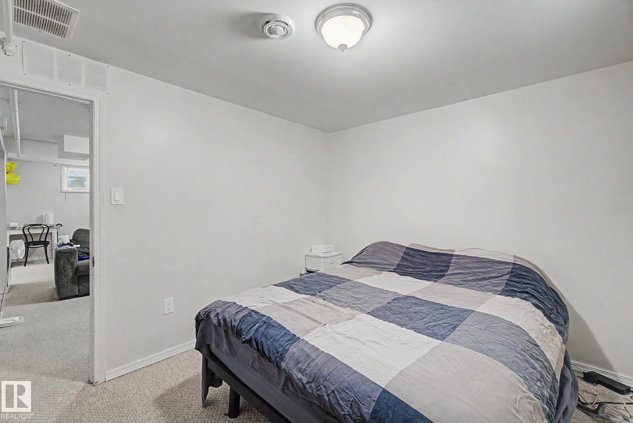 Neutral white walls with a ceiling-mounted light fixture and carpeted flooring - 8710 83 Avenue Nw, Edmonton, AB - Indoor Photo Showing Bedroom