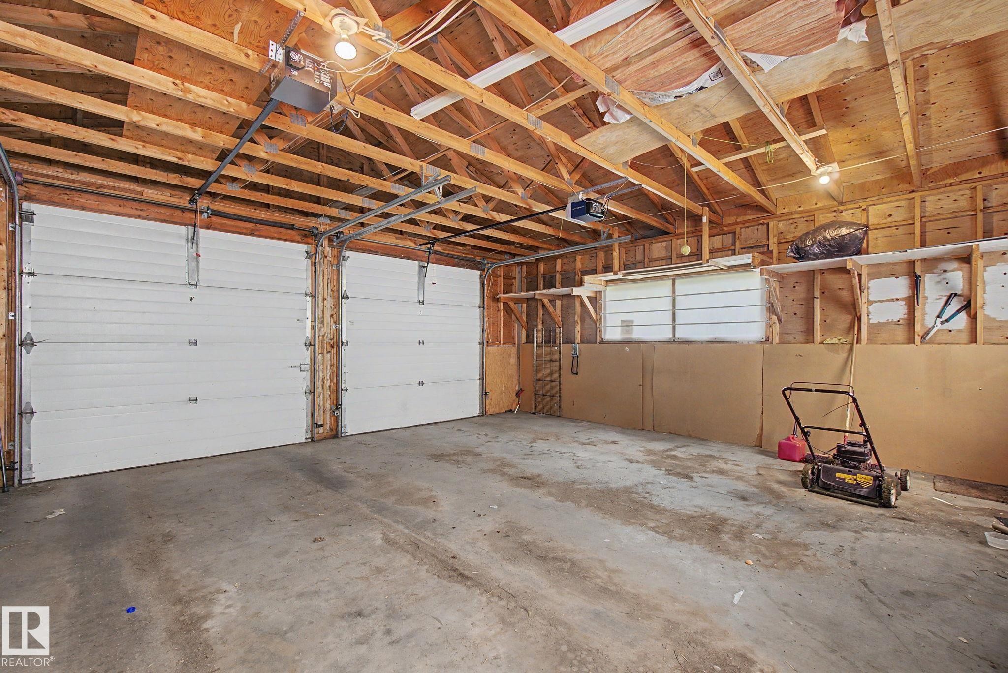 Spacious two-car garage featuring concrete flooring, exposed wood beam ceiling, and two white overhead garage doors - 8710 83 Avenue Nw, Edmonton, AB - Indoor Photo Showing Garage