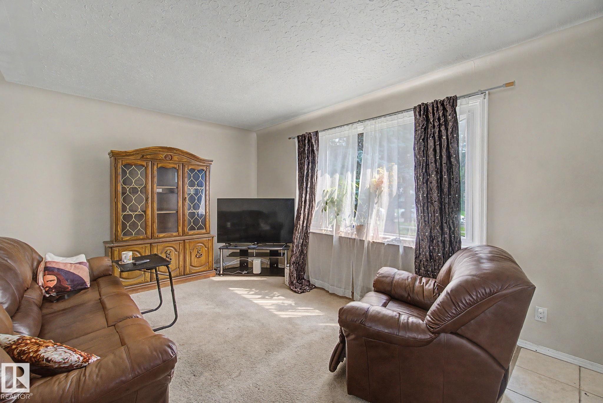 Carpeted living space with a large window, neutral wall paint, and a textured ceiling - 8710 83 Avenue Nw, Edmonton, AB - Indoor Photo Showing Living Room