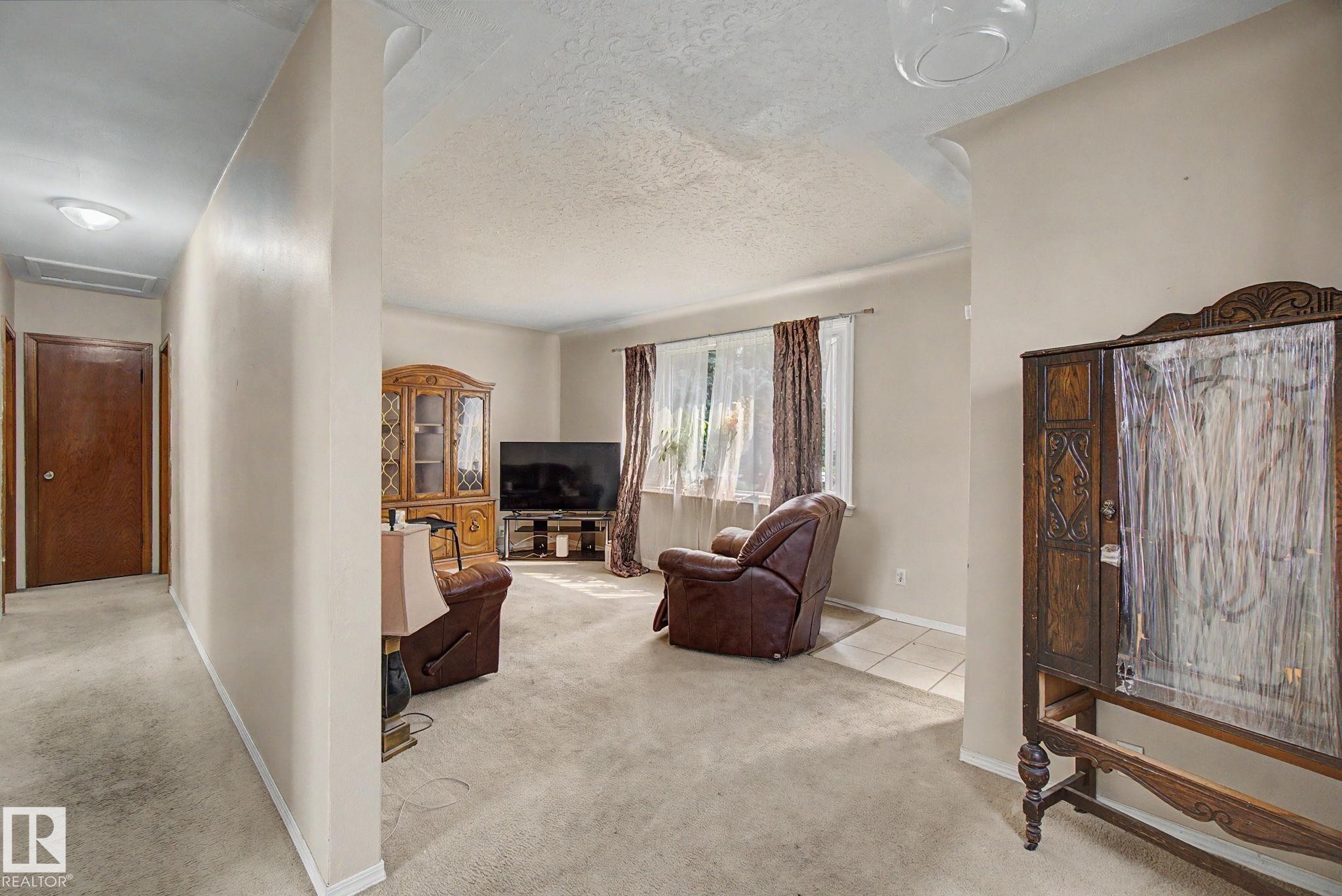 Carpeted living area with a large window and a ceiling-mounted light fixture - 8710 83 Avenue Nw, Edmonton, AB - Indoor