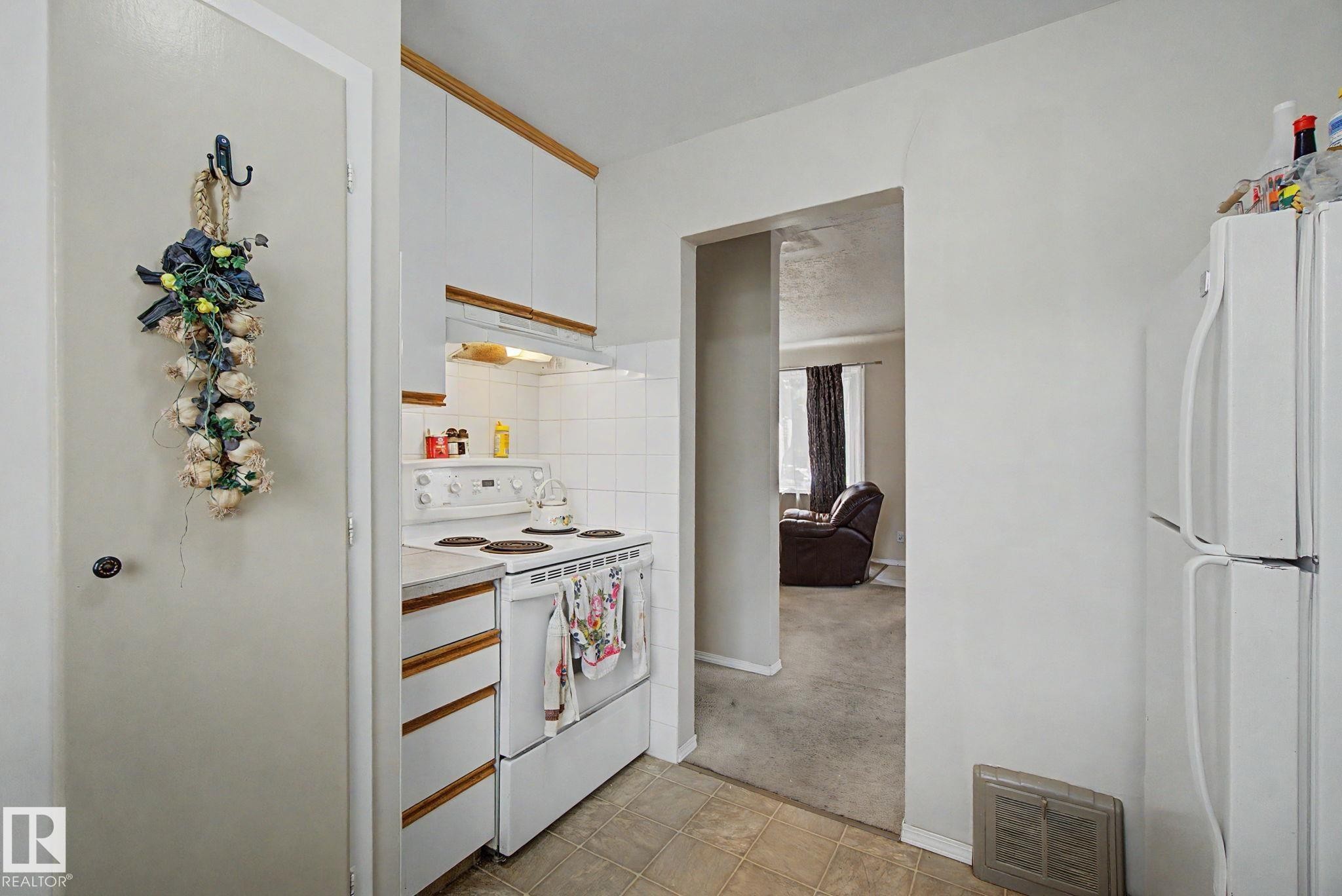 Compact kitchen featuring white cabinetry, white electric range, and a tile backsplash - 8710 83 Avenue Nw, Edmonton, AB - Indoor Photo Showing Kitchen