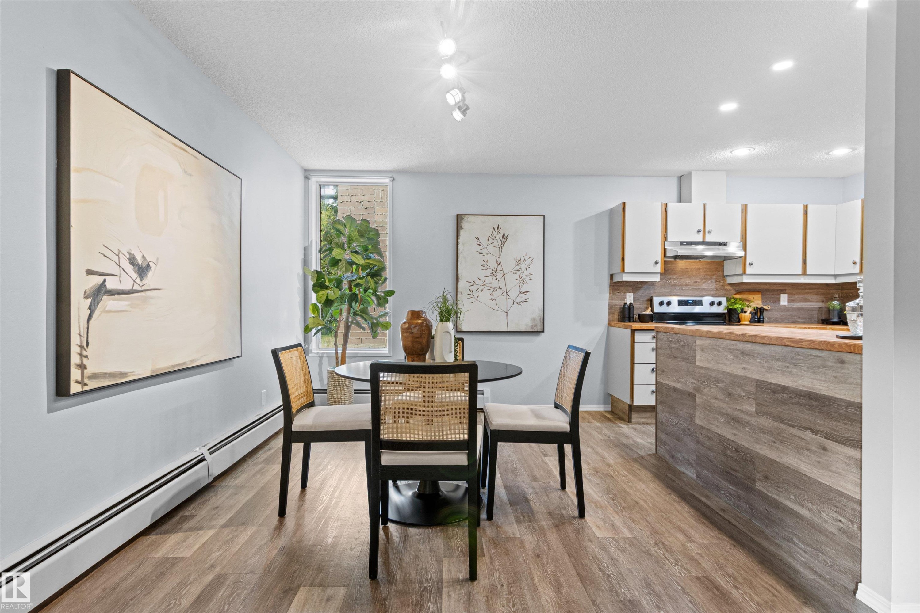 Open-concept living space featuring wood-finish flooring, recessed lighting, a kitchen with white cabinetry, a wood-finish countertop, and a tiled backsplash - #7 10032 113 St Nw, Edmonton, AB
