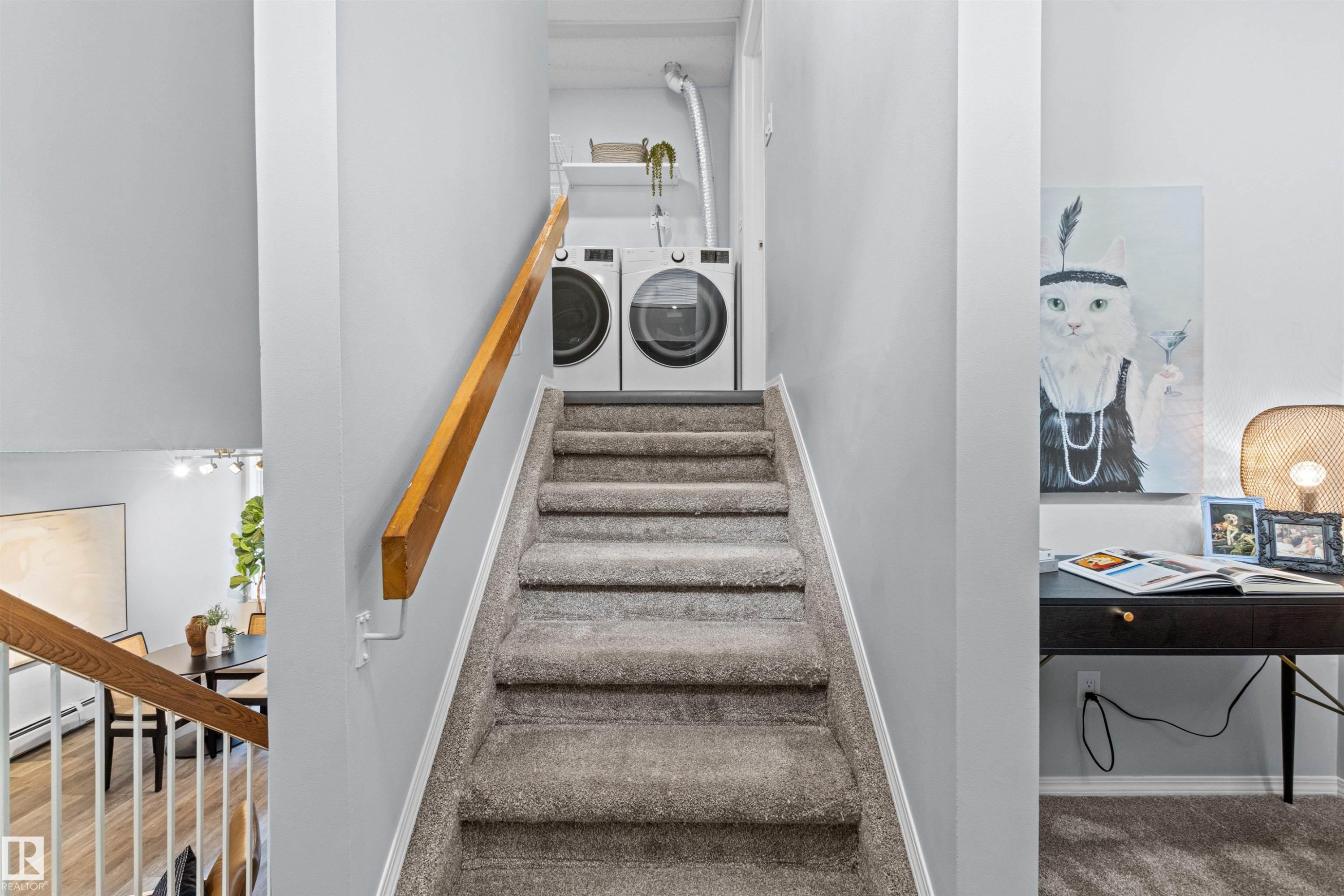 Carpeted staircase with wood-finish handrail leading to a stacked laundry appliance area - #7 10032 113 St Nw, Edmonton, AB