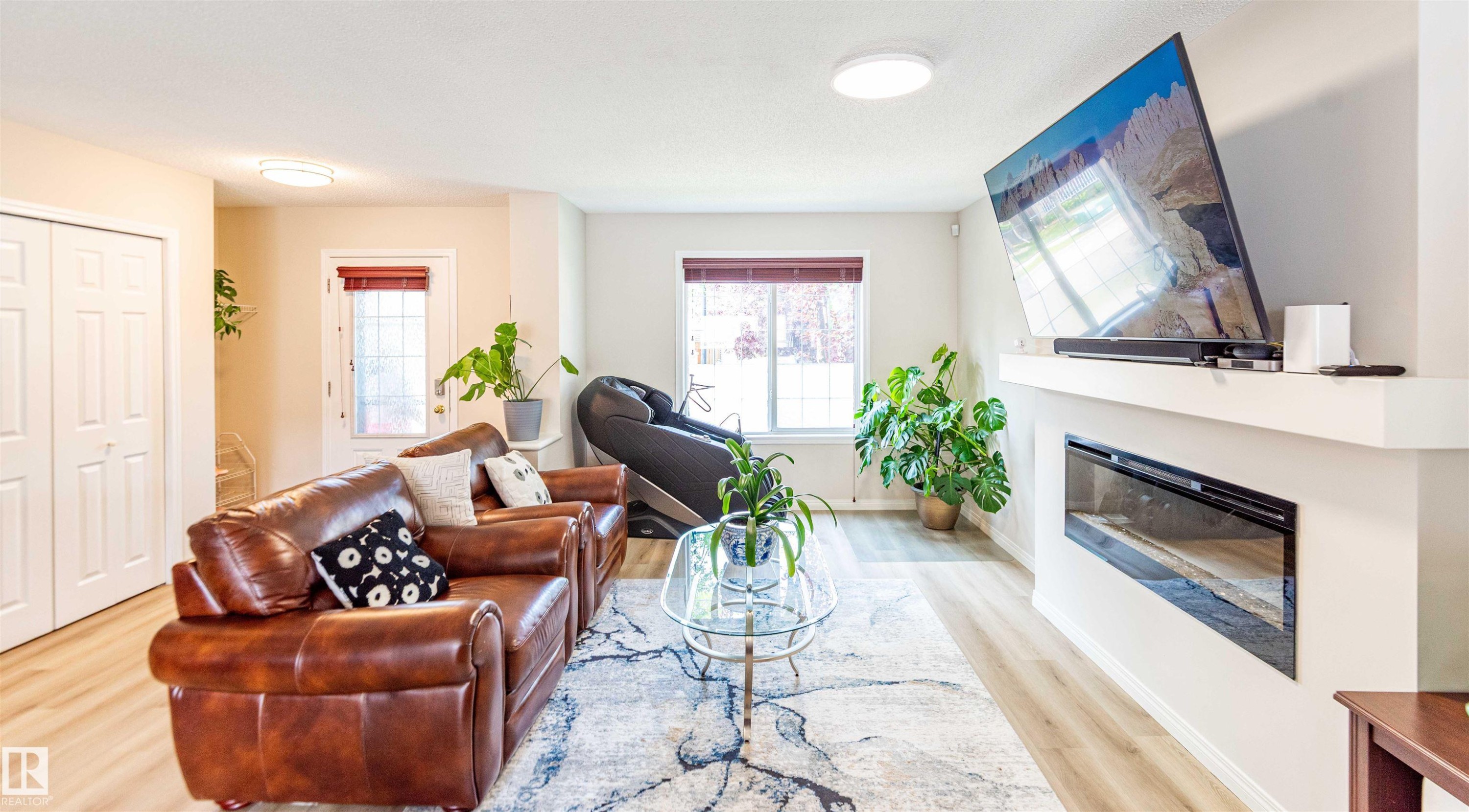 Open-concept living area featuring wood-finish flooring, a contemporary electric fireplace with a white mantel, and bright recessed lighting - 8527 Ellis Link Nw, Edmonton, AB - Indoor Photo Showing Living Room With Fireplace