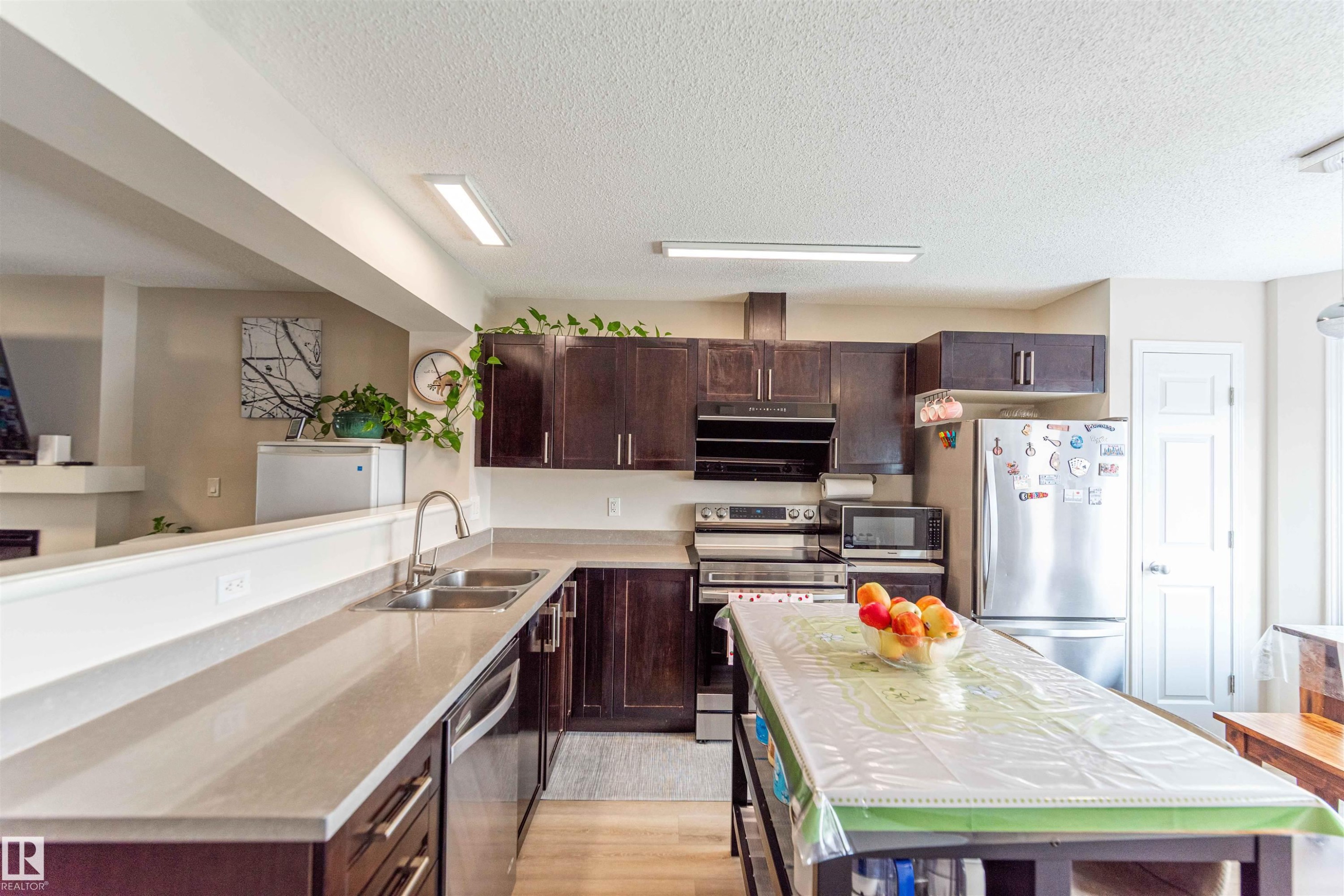 Kitchen featuring dark wood-finish cabinetry, light-toned countertops, and stainless-steel appliances - 8527 Ellis Link Nw, Edmonton, AB - Indoor Photo Showing Kitchen With Double Sink