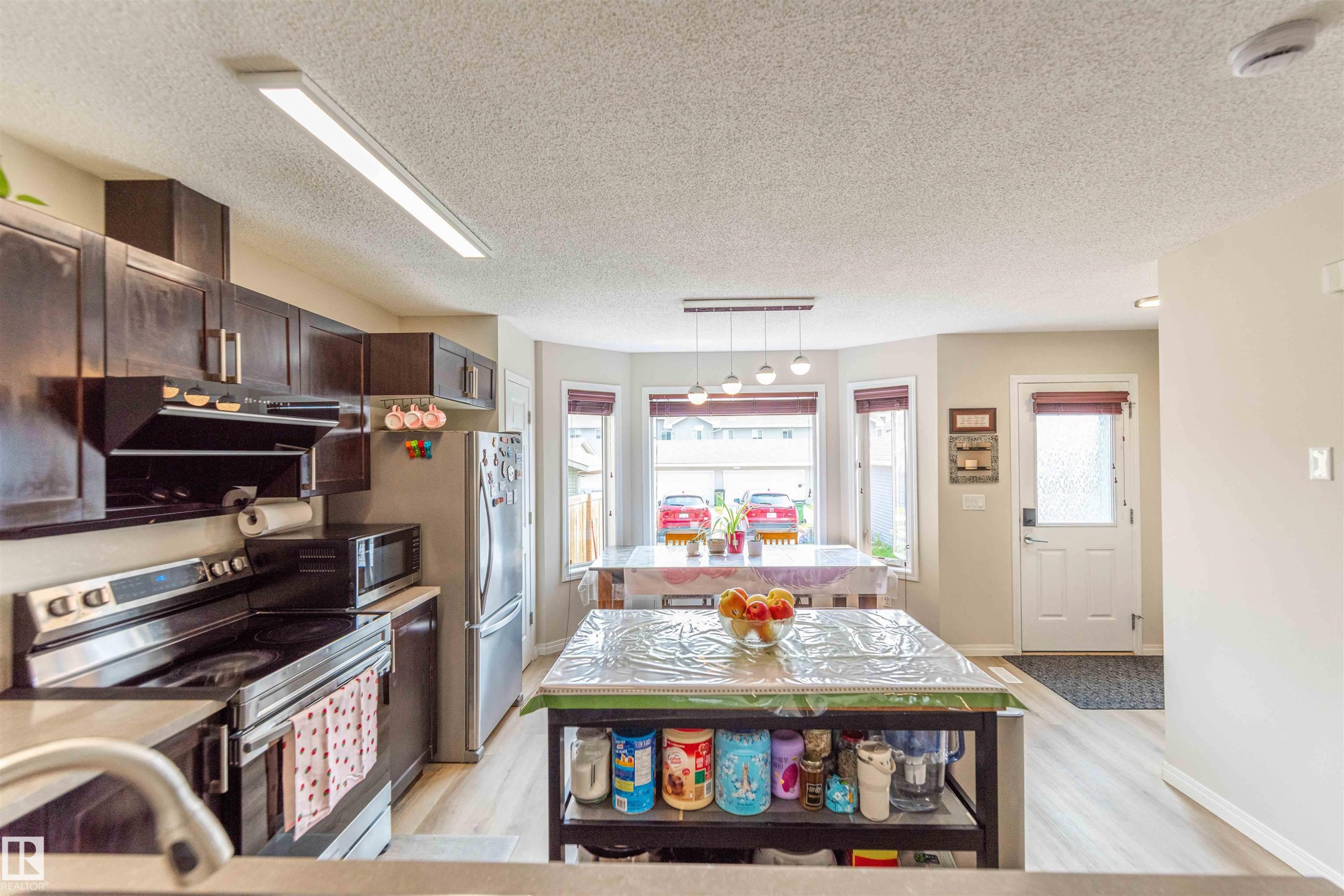 Open-concept kitchen with dark wood cabinetry, stainless steel appliances, light wood-finish flooring, and a bay window dining area - 8527 Ellis Link Nw, Edmonton, AB - Indoor Photo Showing Kitchen