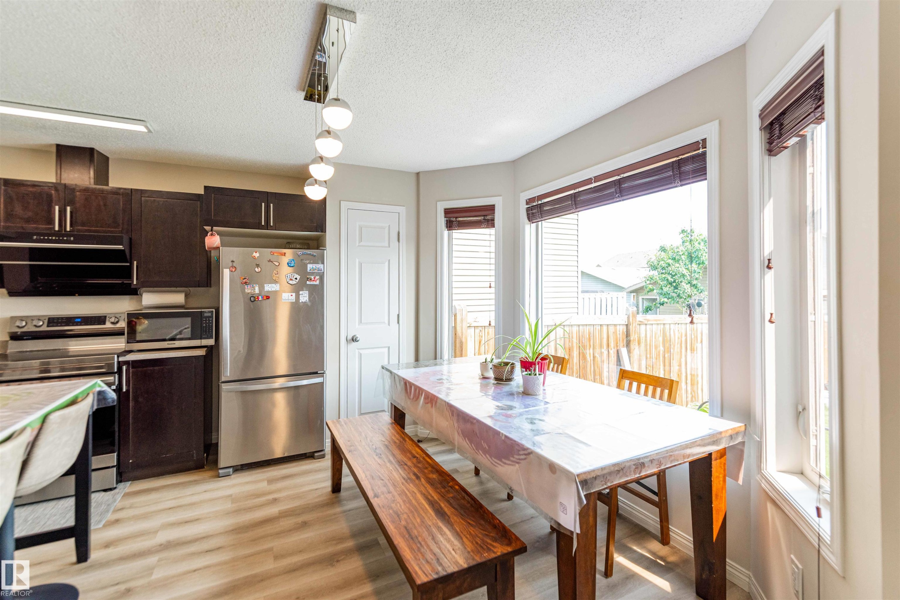 Kitchen and dining area featuring dark wood-finish cabinetry, stainless steel appliances, and wood-finish flooring - 8527 Ellis Link Nw, Edmonton, AB - Indoor Photo Showing Other Room