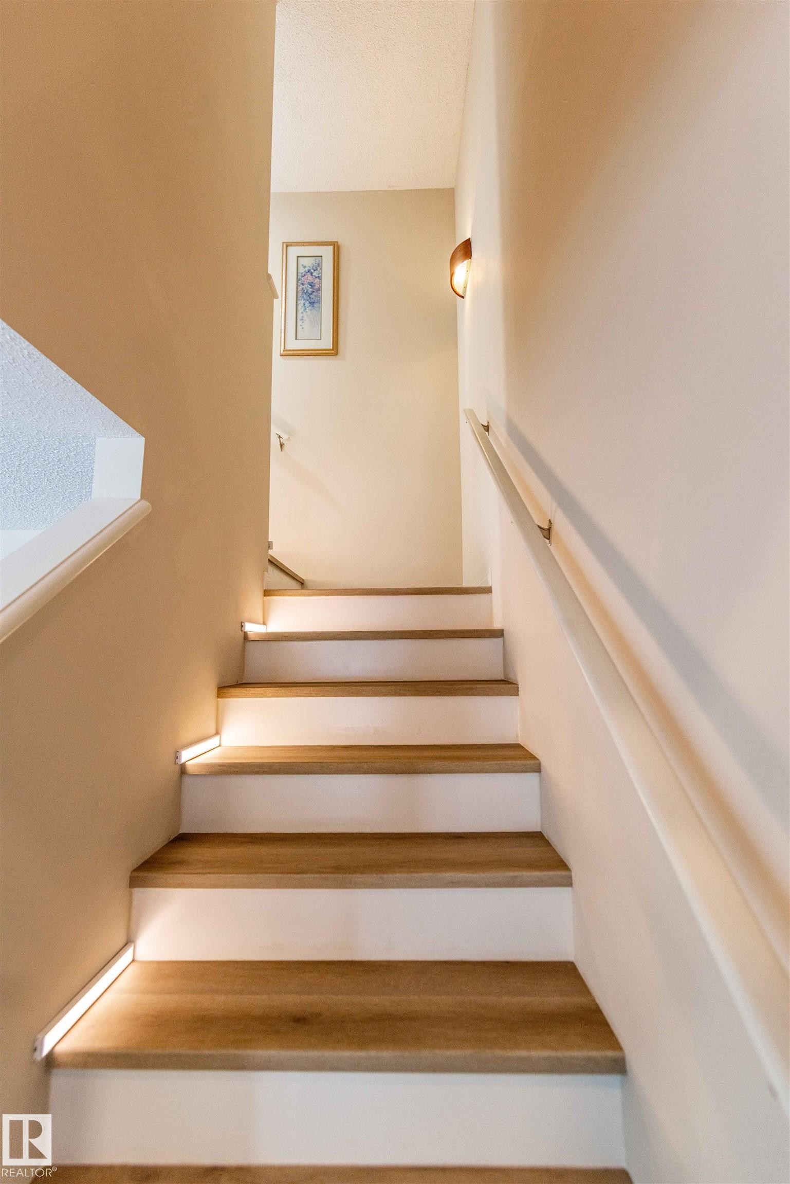 Staircase featuring wood-finish treads, white risers, and contemporary accent lighting - 8527 Ellis Link Nw, Edmonton, AB - Indoor Photo Showing Other Room