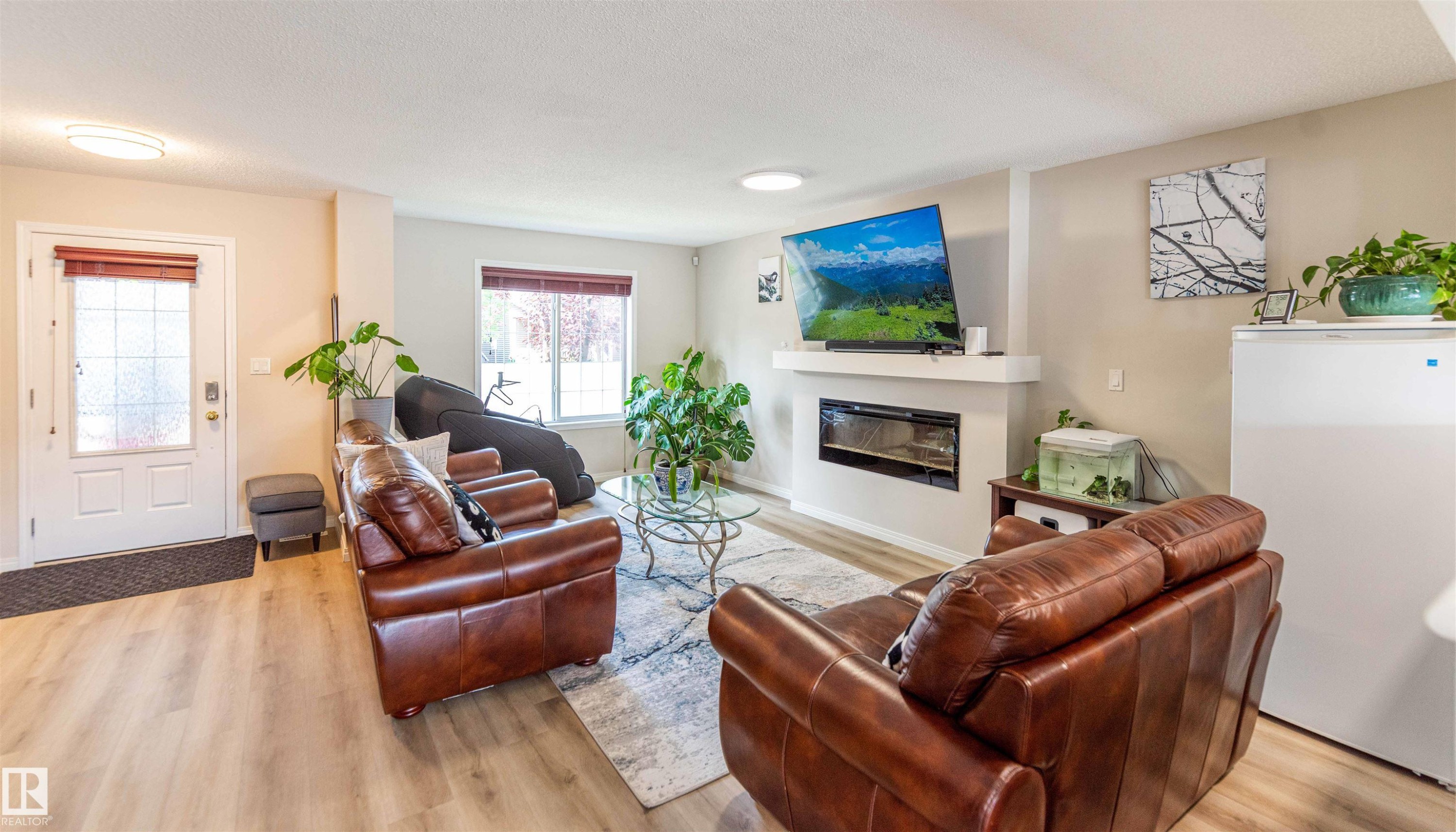 Spacious living area featuring wood-finish flooring, a contemporary electric fireplace with a floating mantel, and a front entry door with decorative glass - 8527 Ellis Link Nw, Edmonton, AB - Indoor Photo Showing Living Room With Fireplace