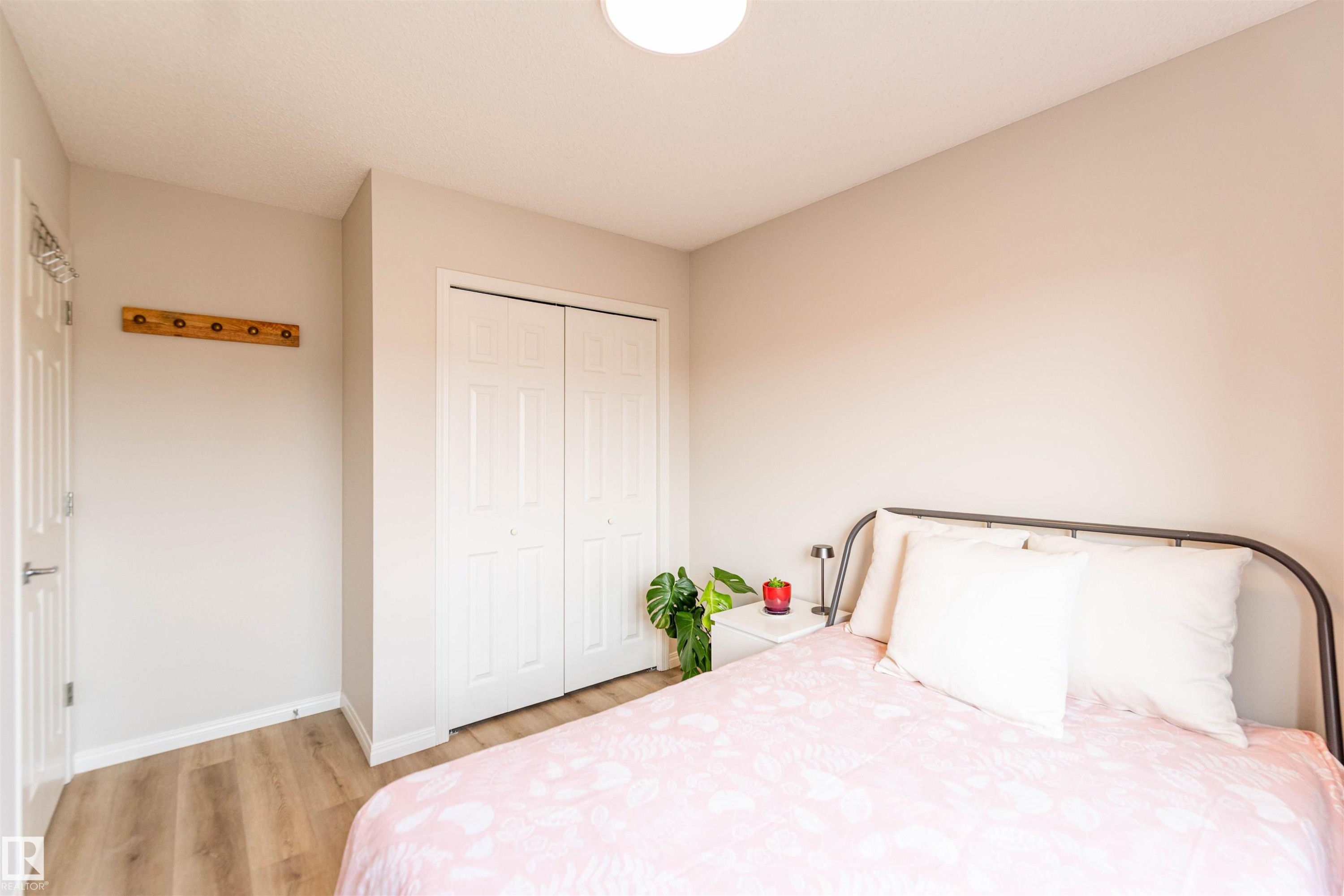 Neutral tone bedroom featuring wood-finish flooring, white baseboards, and a bi-fold closet with panel detailing - 8527 Ellis Link Nw, Edmonton, AB - Indoor Photo Showing Bedroom