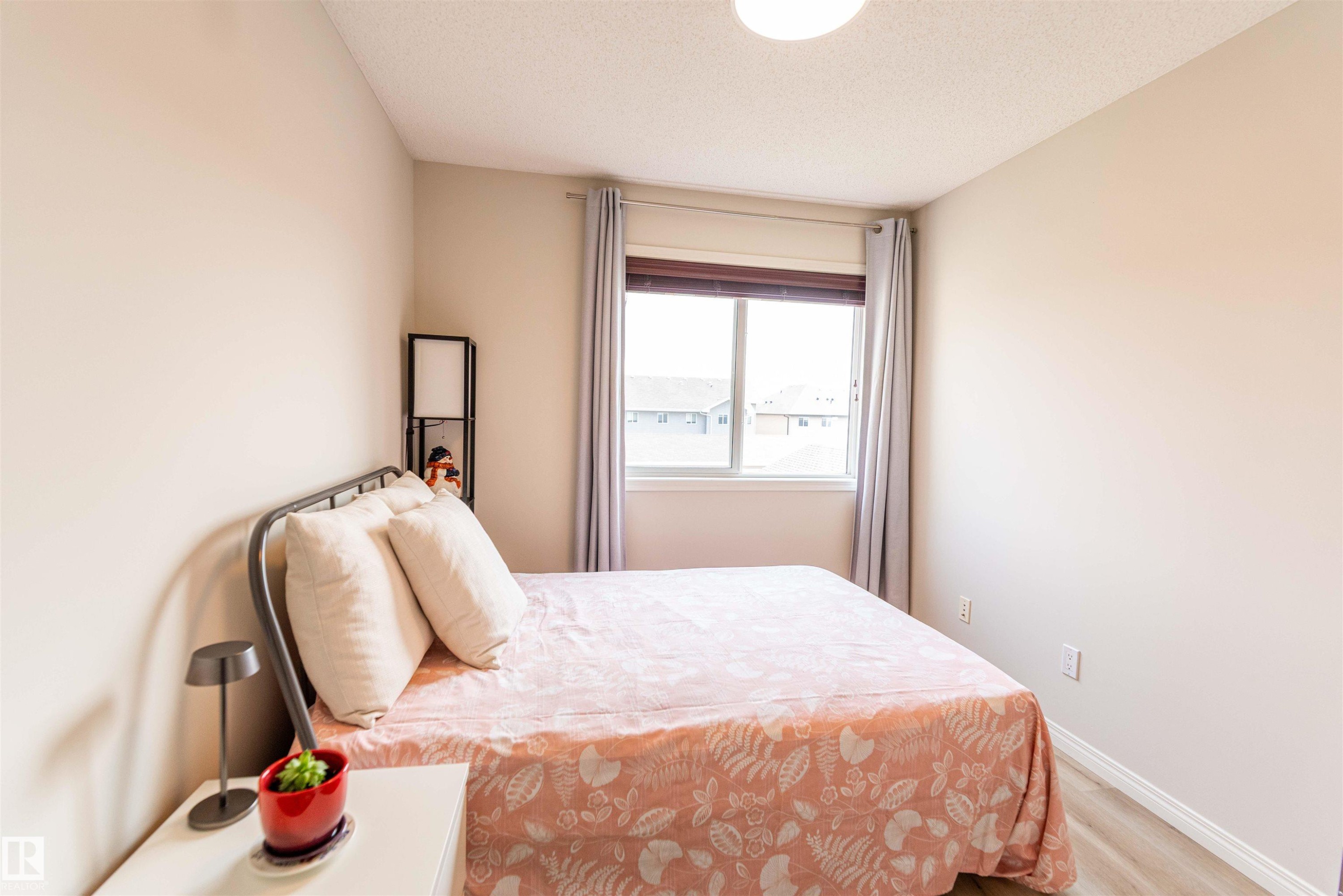 Bedroom featuring a large window with blinds, light wood-finish flooring, neutral wall tones, and a ceiling-mounted light fixture - 8527 Ellis Link Nw, Edmonton, AB - Indoor Photo Showing Bedroom