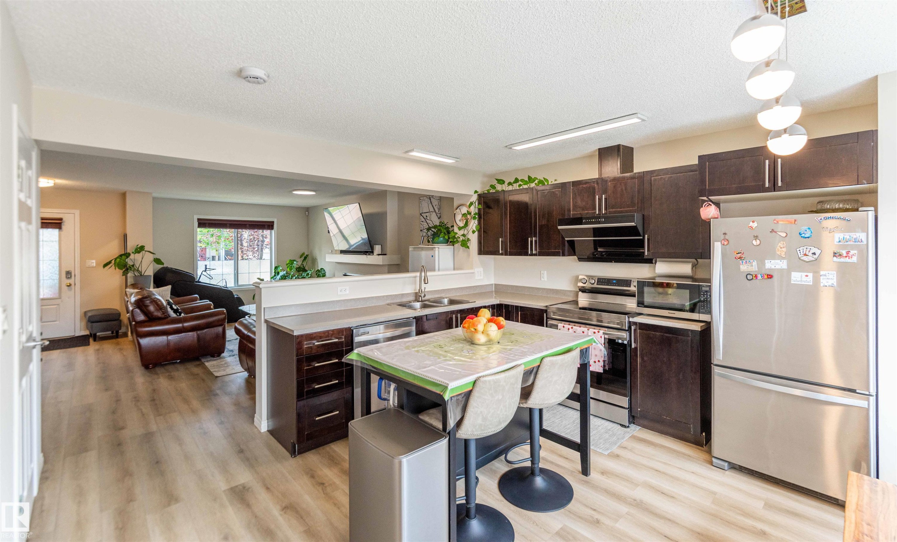Kitchen featuring dark wood cabinetry, stainless steel appliances, a double basin sink, and wood-finish flooring - 8527 Ellis Link Nw, Edmonton, AB - Indoor Photo Showing Kitchen With Double Sink