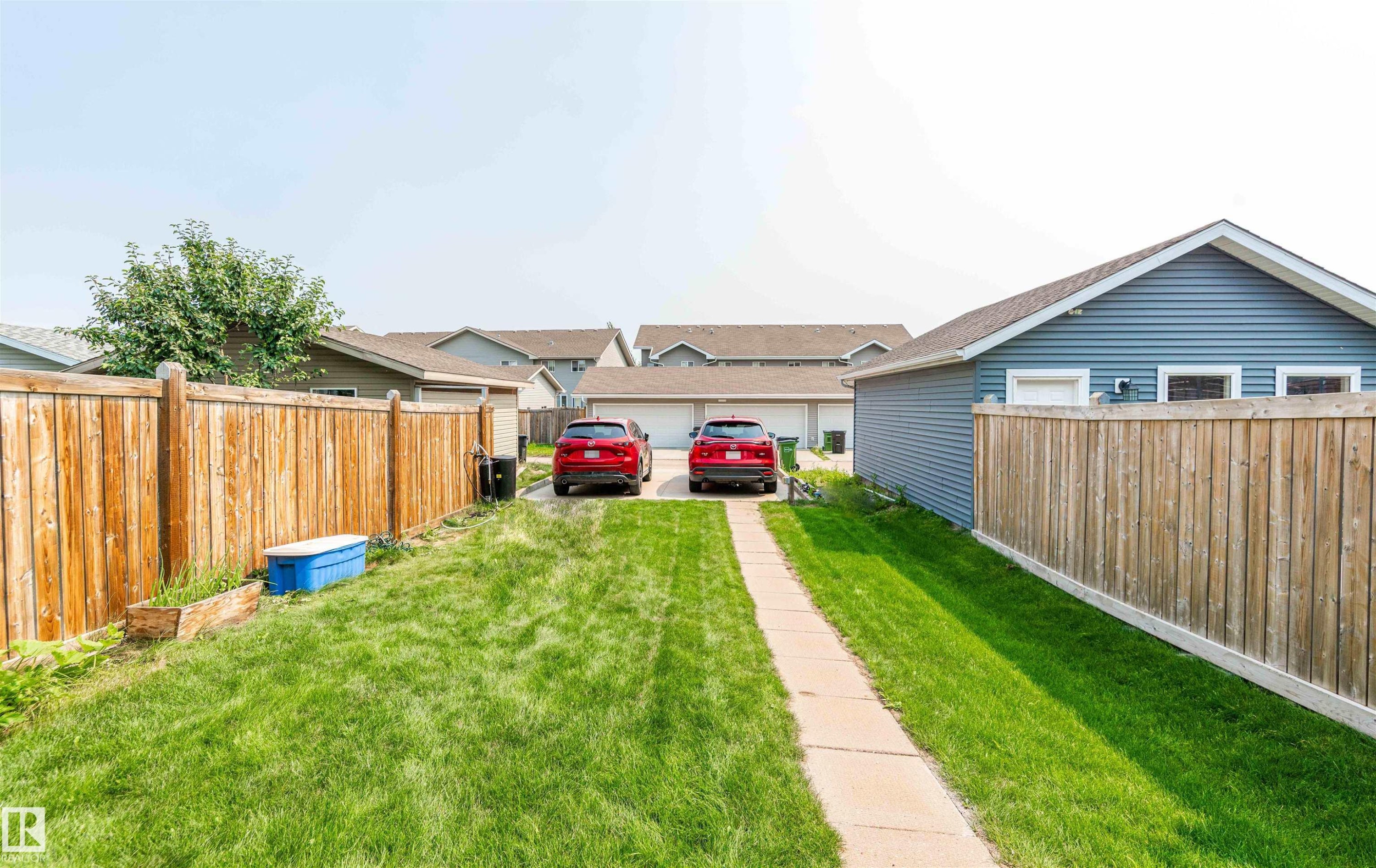 Expansive backyard featuring a concrete pathway, a detached blue-sided garage, and a wood privacy fence - 8527 Ellis Link Nw, Edmonton, AB - Outdoor