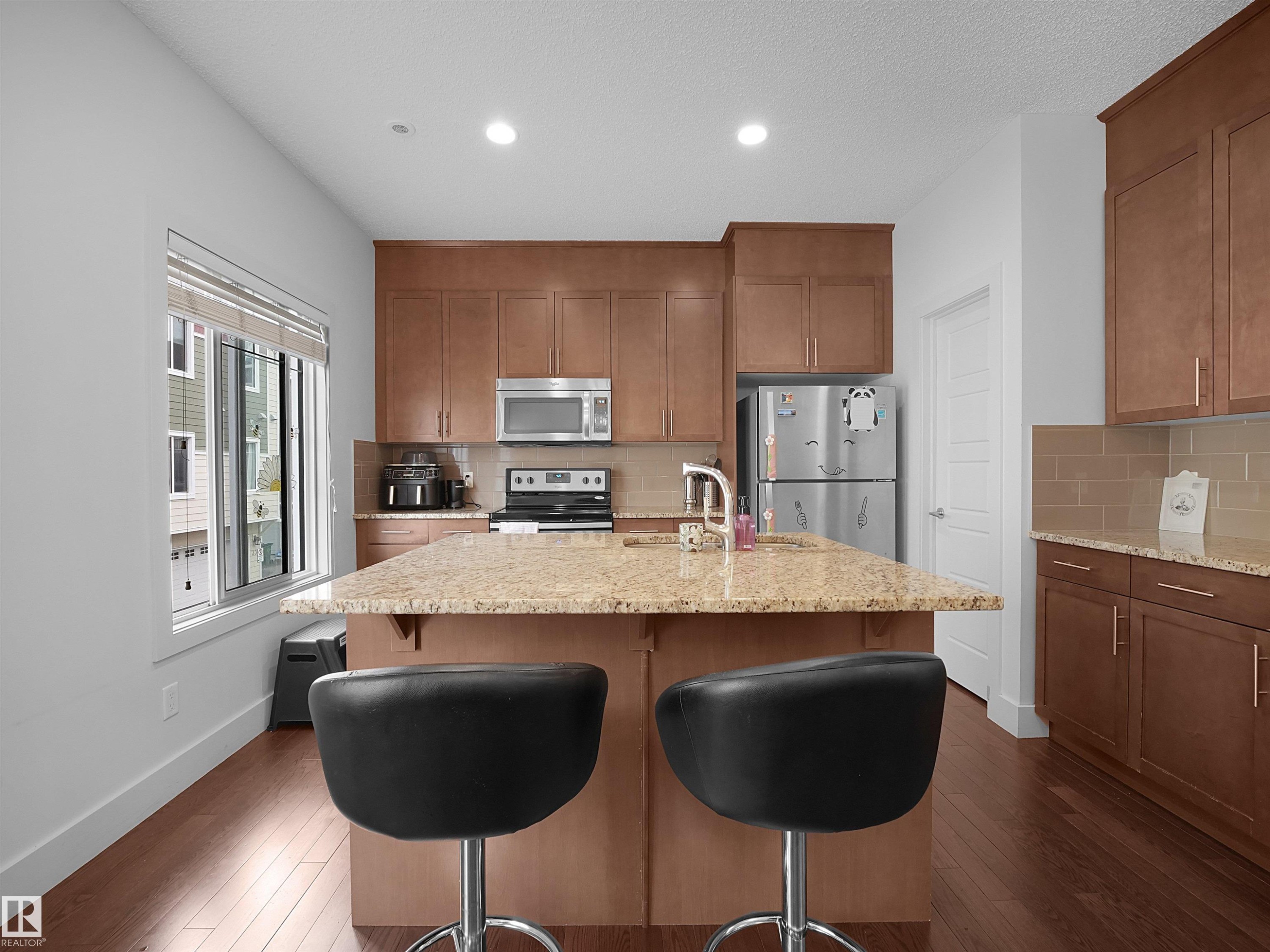 Kitchen featuring a central island with countertop seating, wood-finish flooring, stainless steel appliances, and wood cabinetry - #40 2003 Rabbit Hill Rd Nw, Edmonton, AB