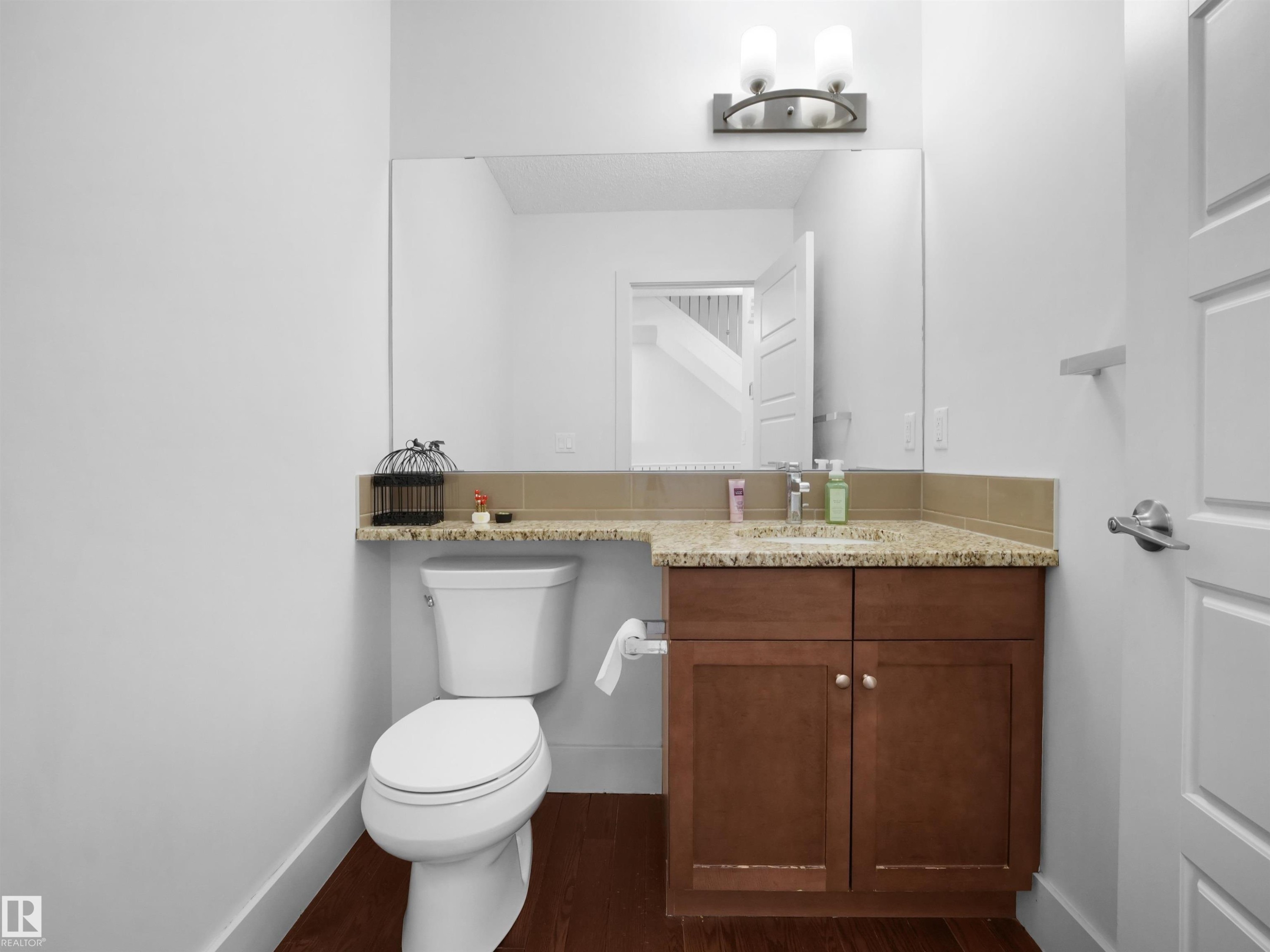 Powder room featuring a vanity with a light-colored stone countertop, wood-finish cabinetry, a built-in sink, and a large wall-mounted mirror - #40 2003 Rabbit Hill Rd Nw, Edmonton, AB