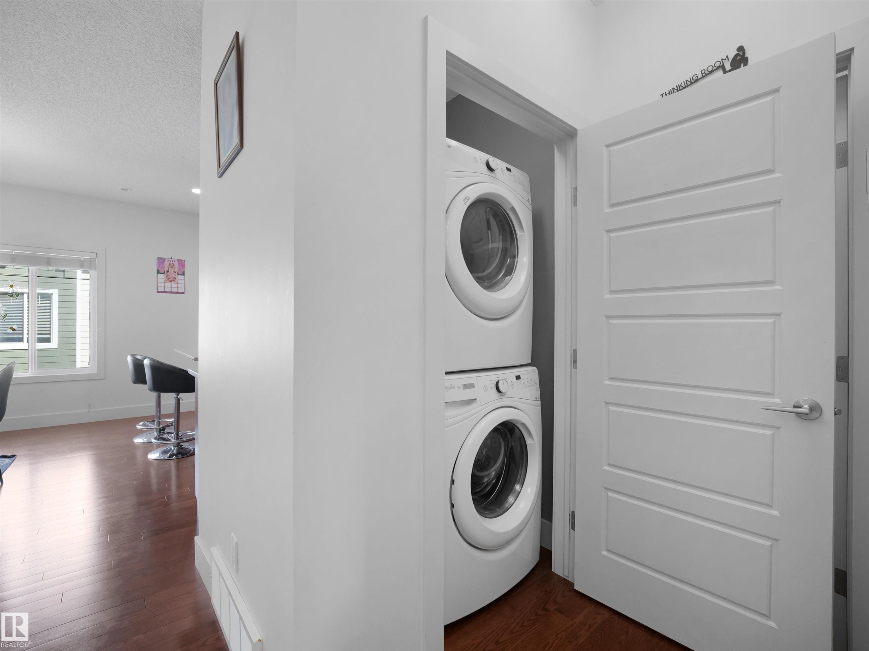 Stackable washer and dryer appliances, wood-finish flooring, white trim, and a contemporary panel door - #40 2003 Rabbit Hill Rd Nw, Edmonton, AB