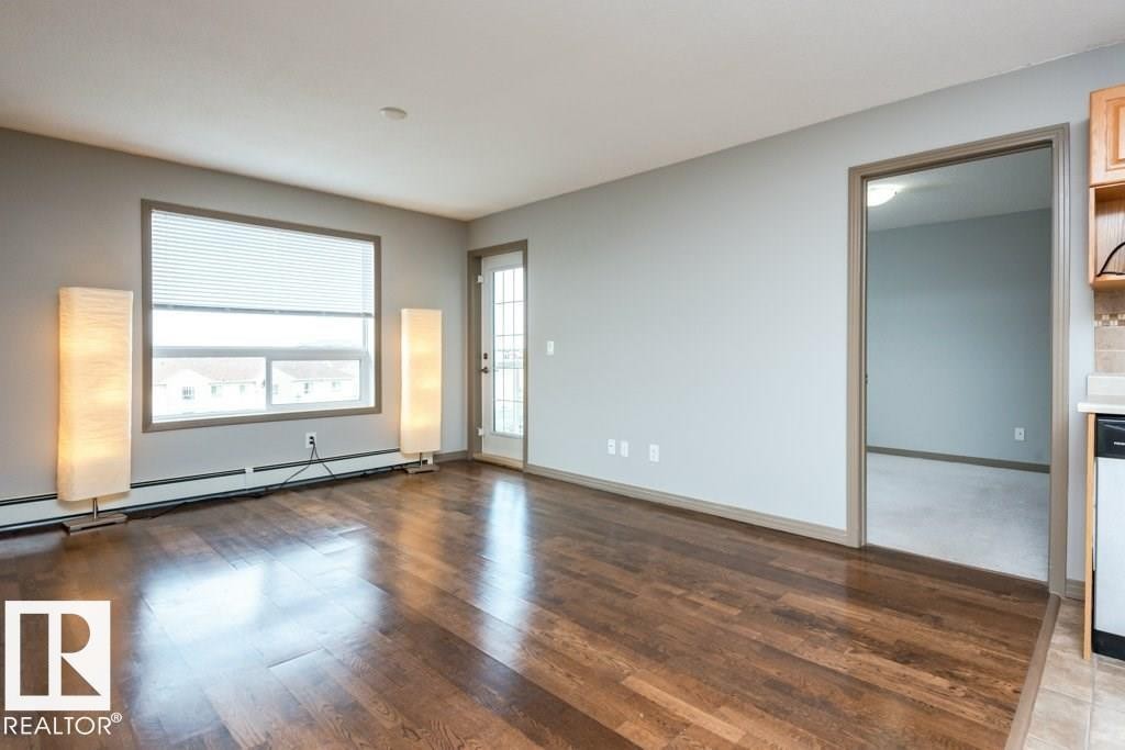 Wood-finish flooring throughout, light gray wall finishes, and a window with horizontal blinds - 401 5005 165 Avenue Nw, Edmonton, AB
