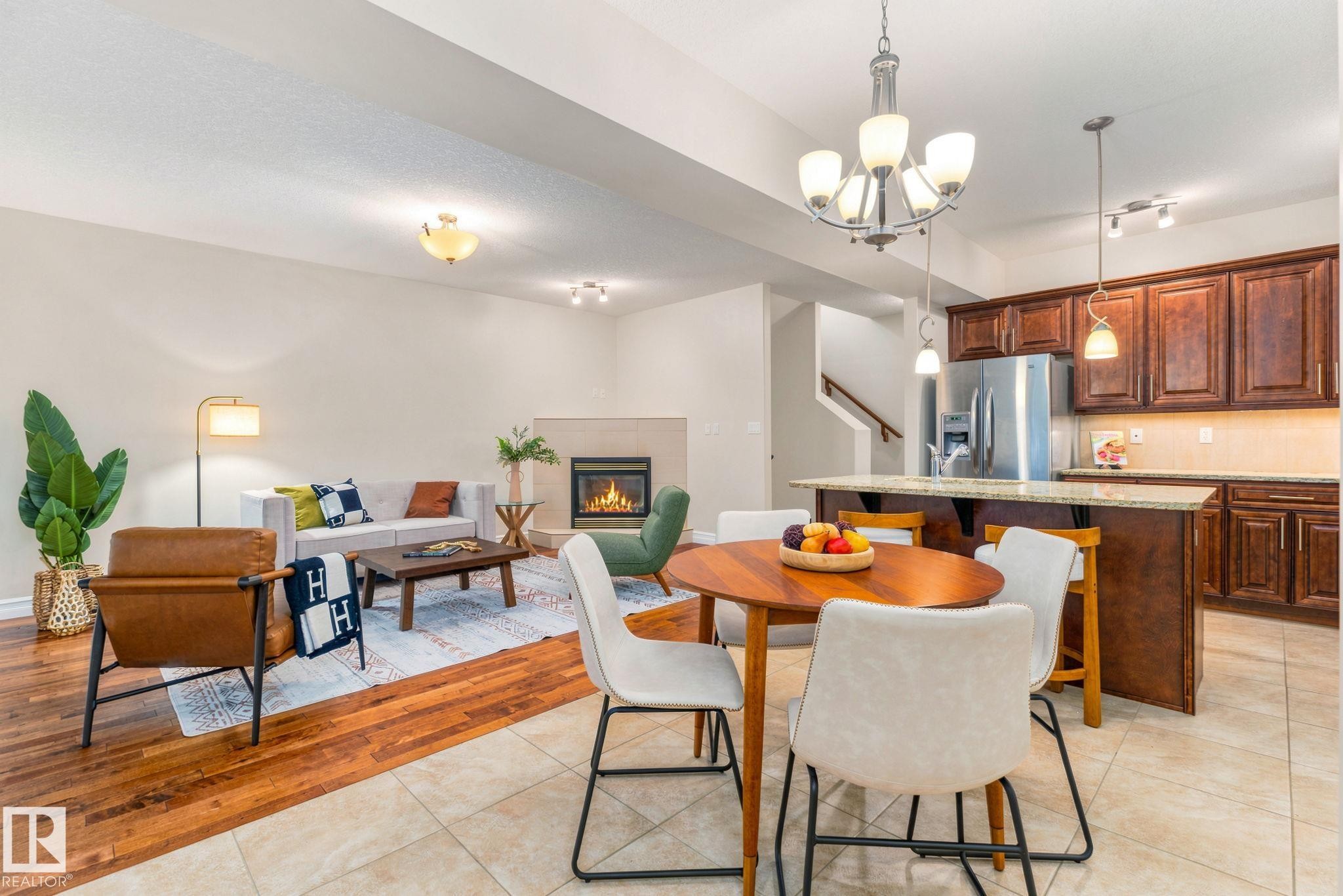 Open-concept living area with wood-finish flooring, a tiled fireplace, and a kitchen featuring wood cabinetry, stainless steel appliances, and a breakfast bar with pendant lighting - 10143 123 Street Nw, Edmonton, AB