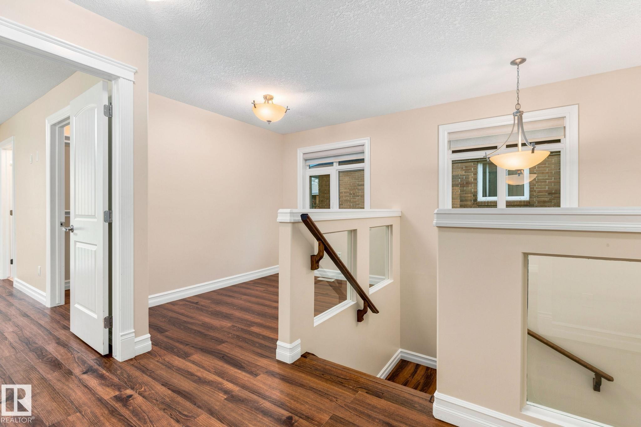 Wood-finish flooring throughout, white trim, recessed staircase with wood handrail, and contemporary pendant lighting - 10143 123 Street Nw, Edmonton, AB