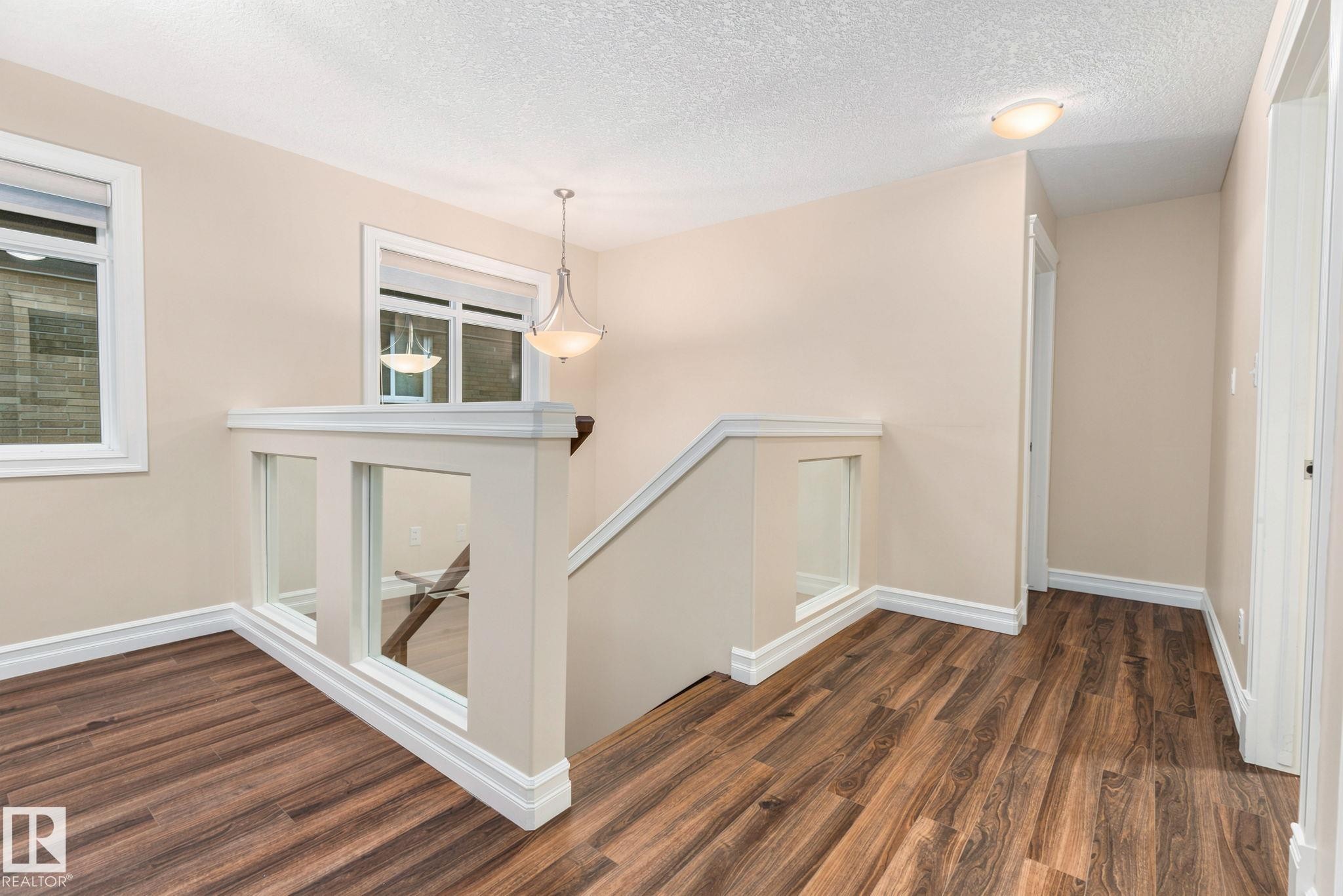 Wood-finish flooring, contemporary glass panel railing, white trim details, recessed lighting, and a decorative pendant light fixture - 10143 123 Street Nw, Edmonton, AB