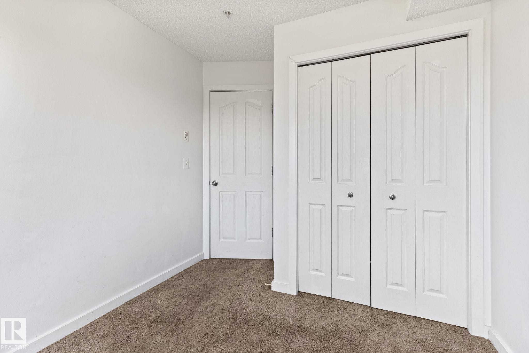 Neutral wall paint, textured carpet, white interior door, and bi-fold closet doors - #306 530 Watt Bv Sw, Edmonton, AB