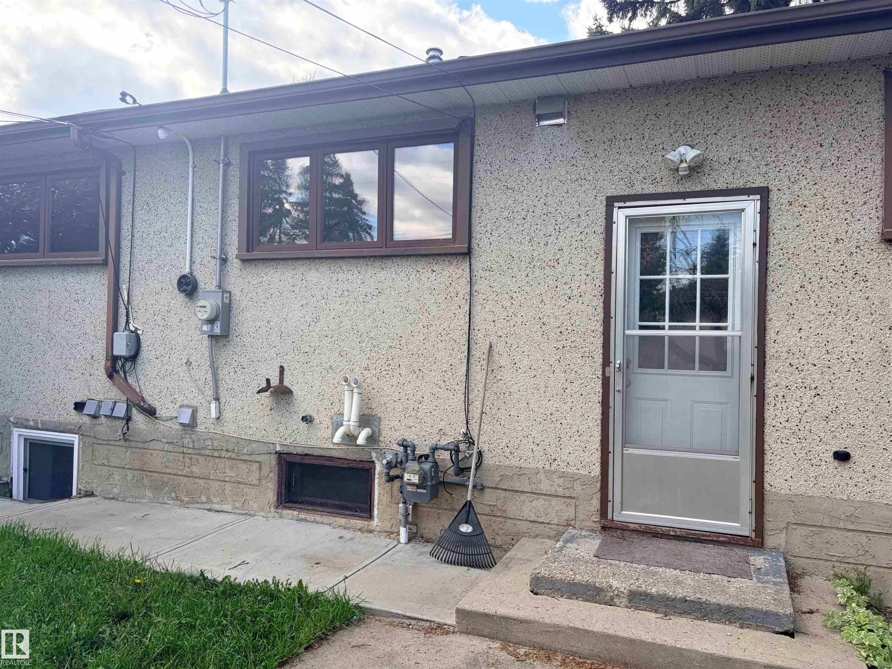 Textured exterior finish with multiple windows, a storm door, and a concrete pathway - 13219 107 Street Nw, Edmonton, AB