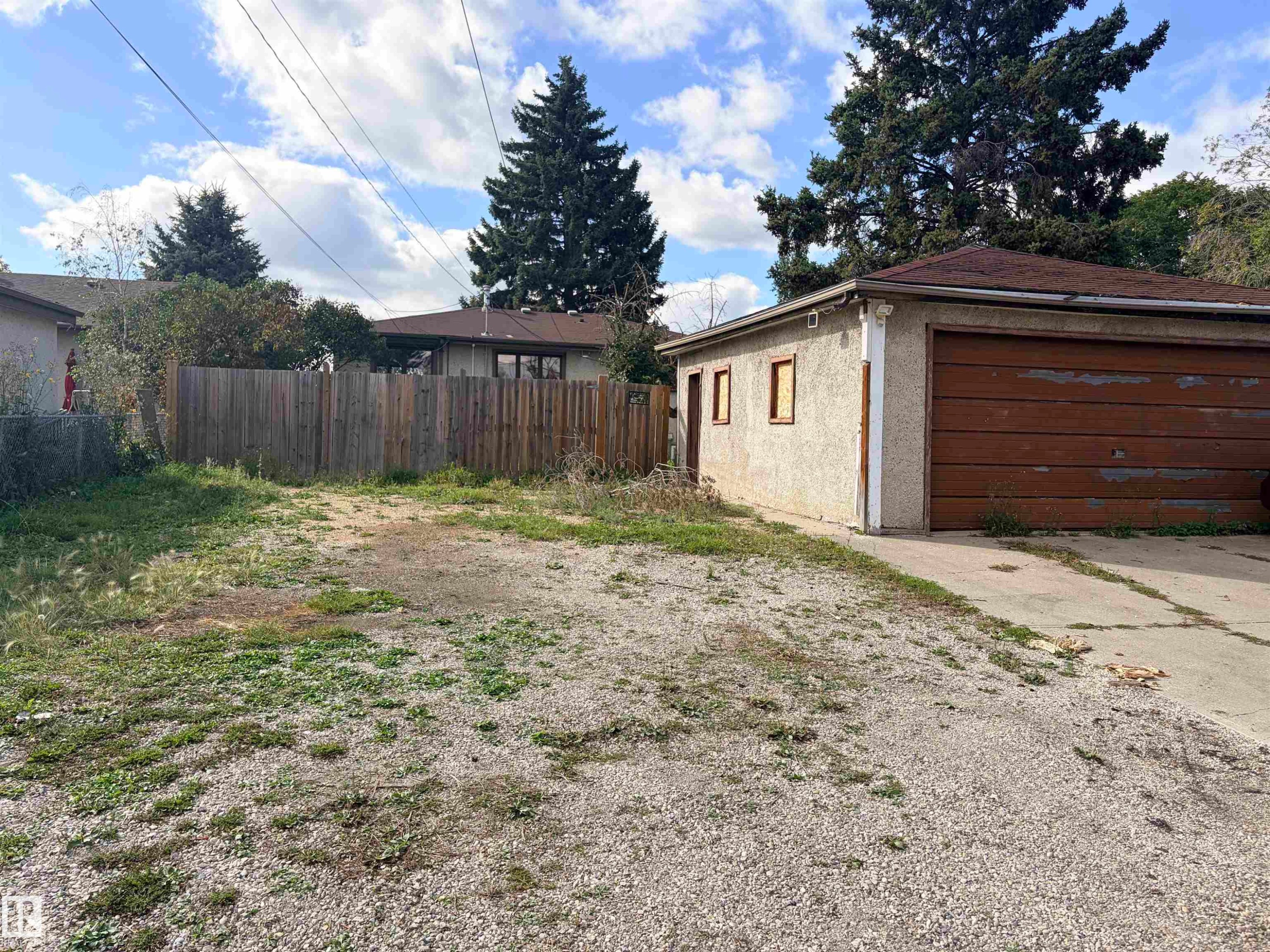 Detached garage with a wood-finish overhead door, stucco exterior, and a gravel driveway - 13219 107 Street Nw, Edmonton, AB