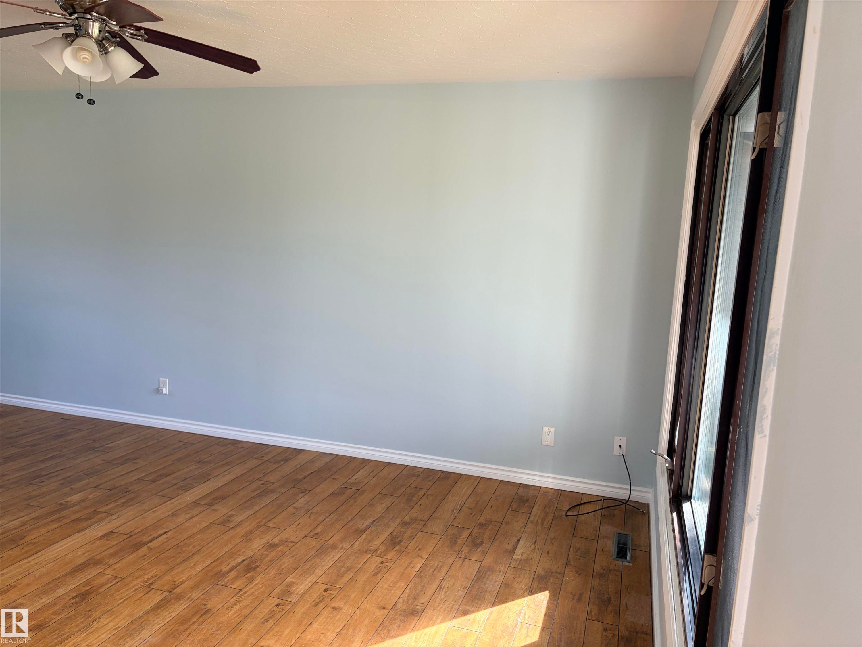 Wood-finish flooring, light blue wall paint, a ceiling fan with integrated lighting, and a dark-framed window - 13219 107 Street Nw, Edmonton, AB