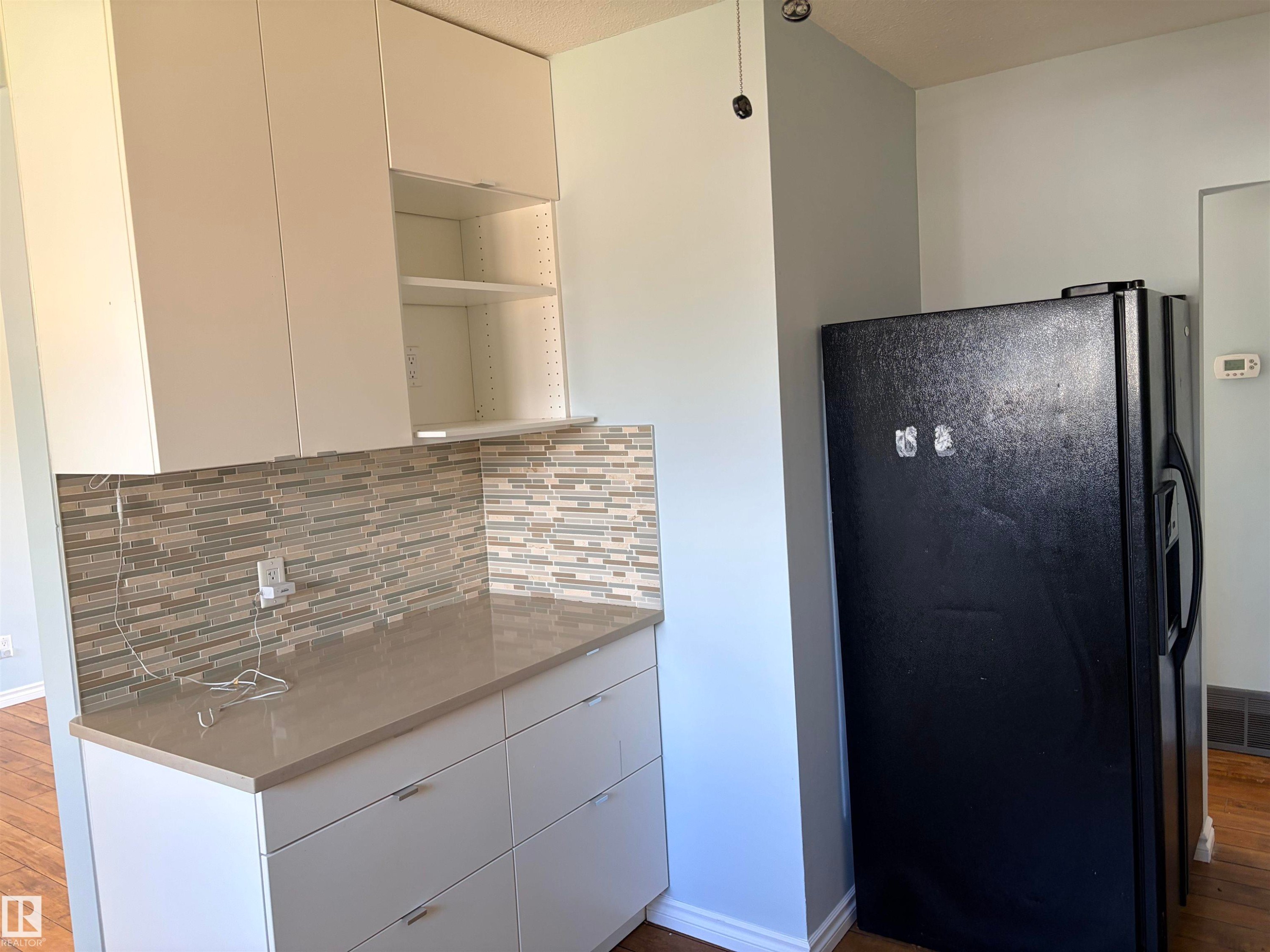 White upper and lower cabinetry with sleek hardware, light-toned countertop, and a mosaic tile backsplash - 13219 107 Street Nw, Edmonton, AB