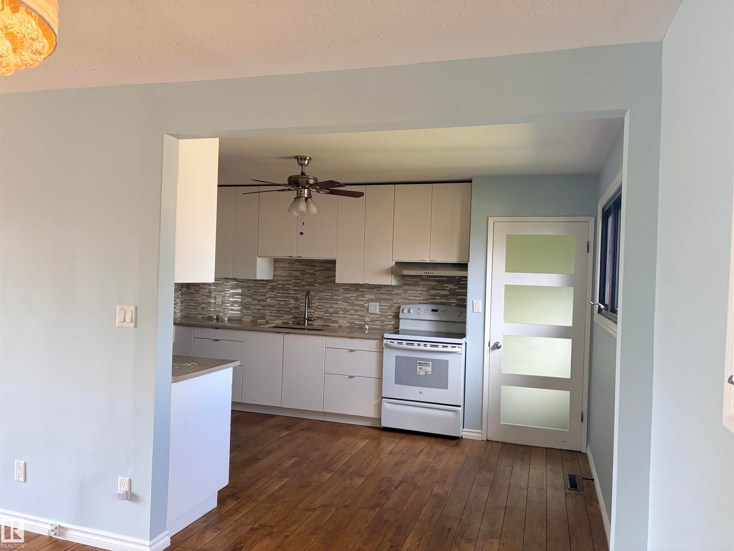 Wood-finish flooring, white cabinetry, tile backsplash, built-in ceiling fan, and a white paneled door with frosted glass inserts Upstairs kitchen - 13219 107 Street Nw, Edmonton, AB