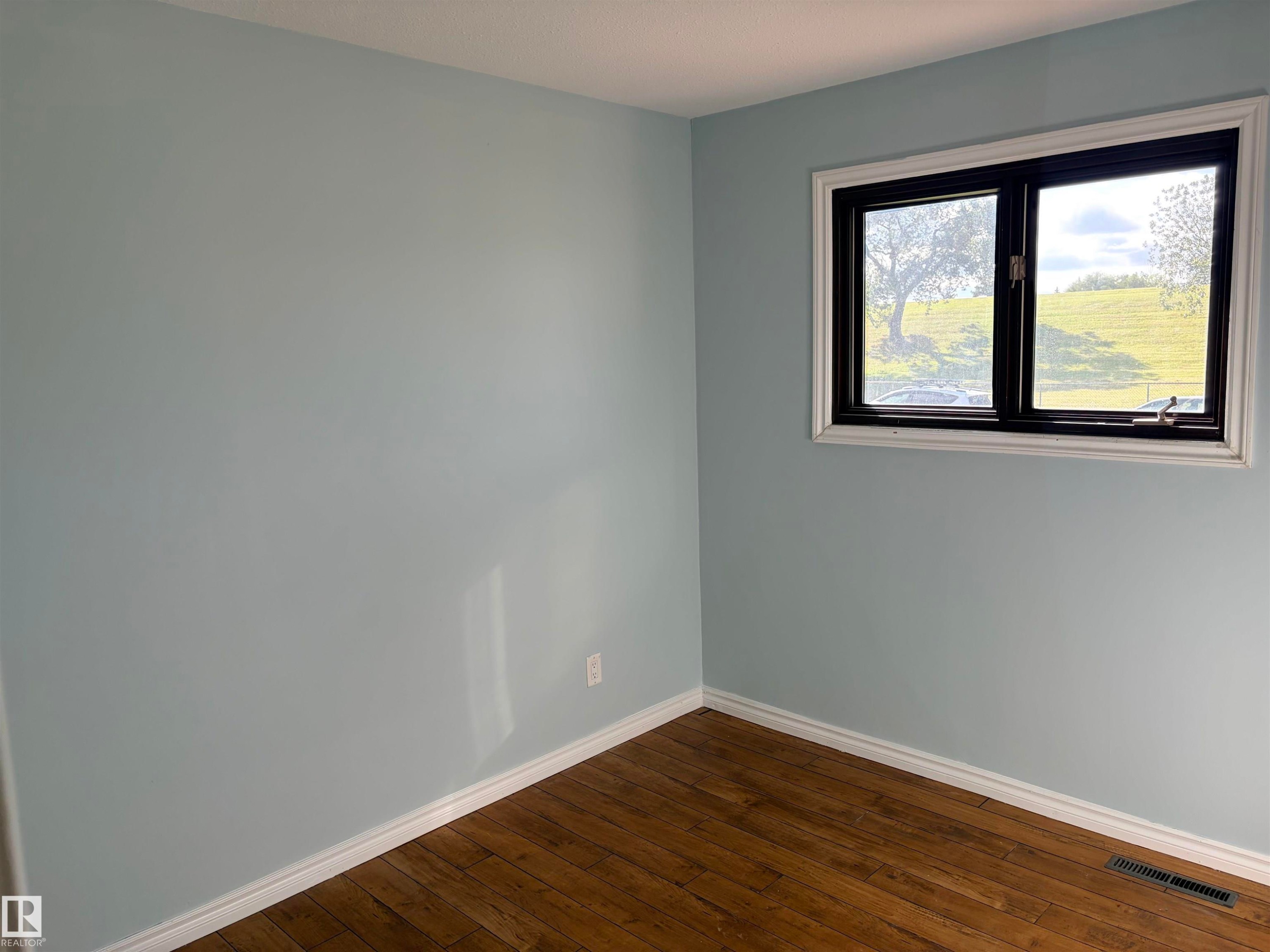 Wood-finish flooring, light blue wall color, white trim, and a window with black framing. Lots of natural light . - 13219 107 Street Nw, Edmonton, AB