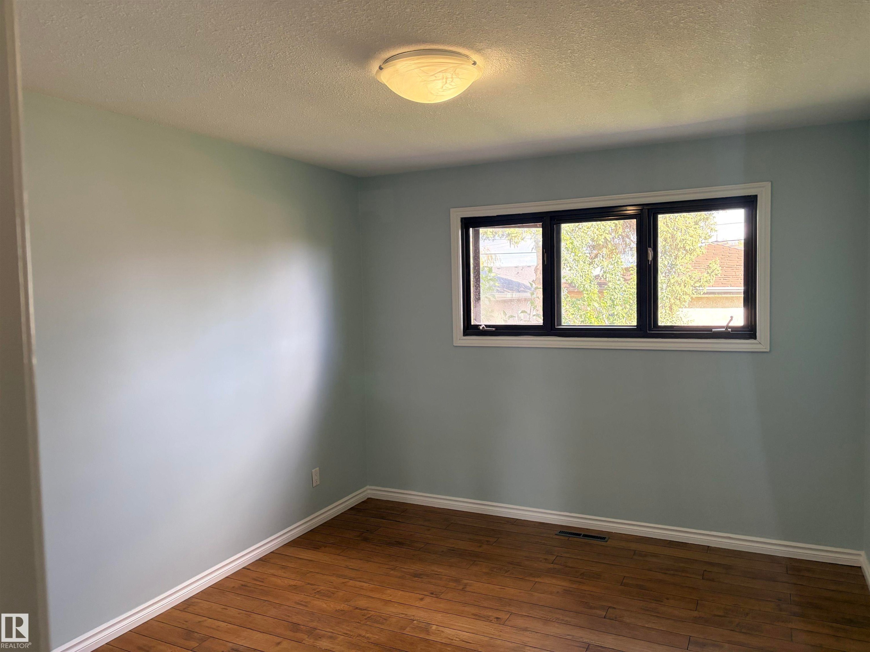 Wood-finish flooring with white trim, light blue wall paint, and a multi-pane window with dark framing bedroom 3 upstairs - 13219 107 Street Nw, Edmonton, AB