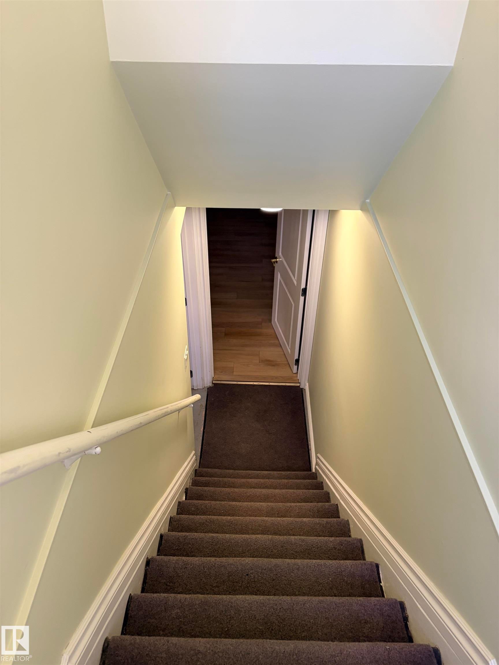 Staircase with carpeted treads, a white handrail, and light-toned wall finishes Leads to basement suite. - 13219 107 Street Nw, Edmonton, AB