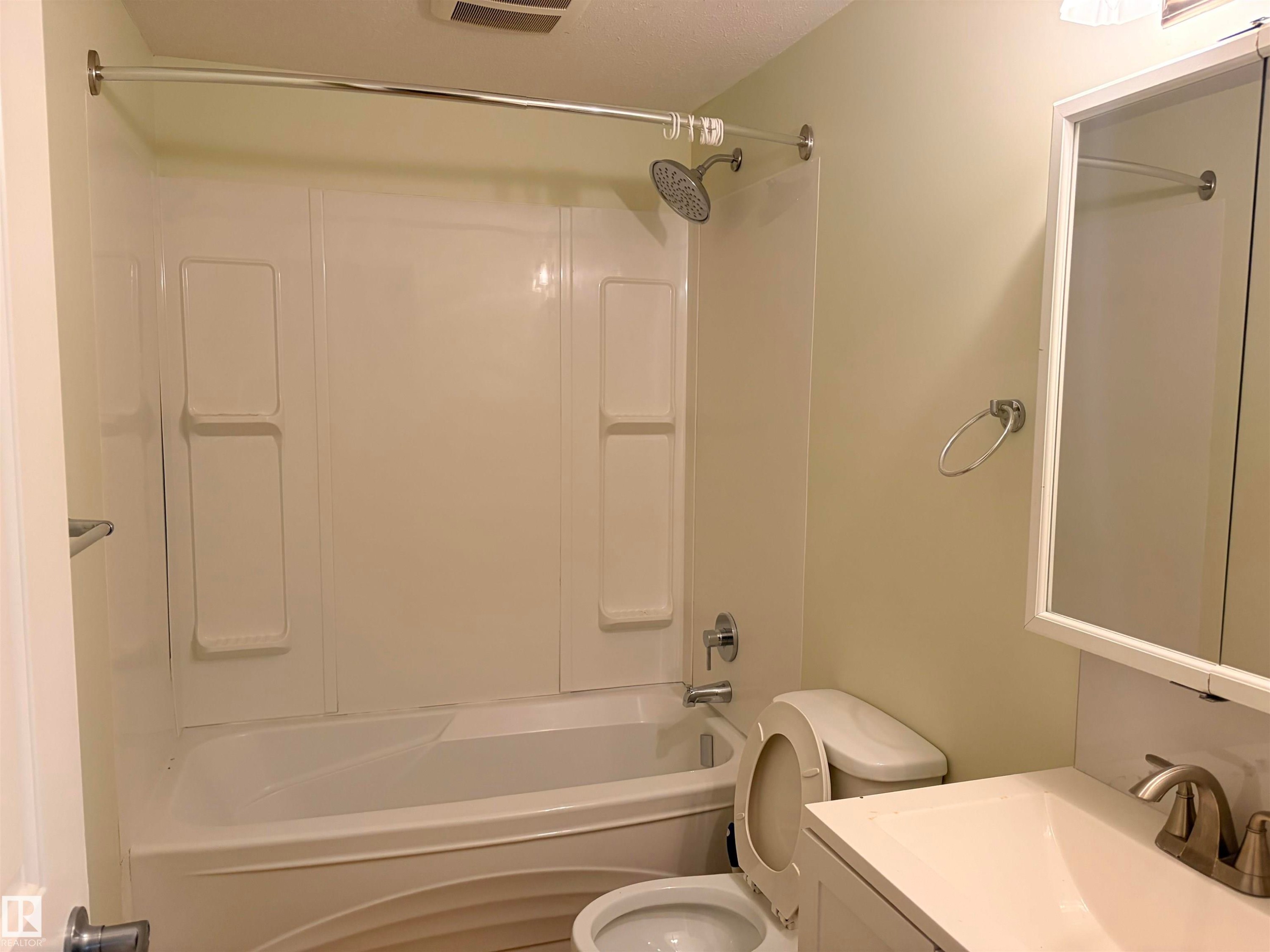 White bath and shower combination with a curved shower curtain rod, basement bathroom. - 13219 107 Street Nw, Edmonton, AB