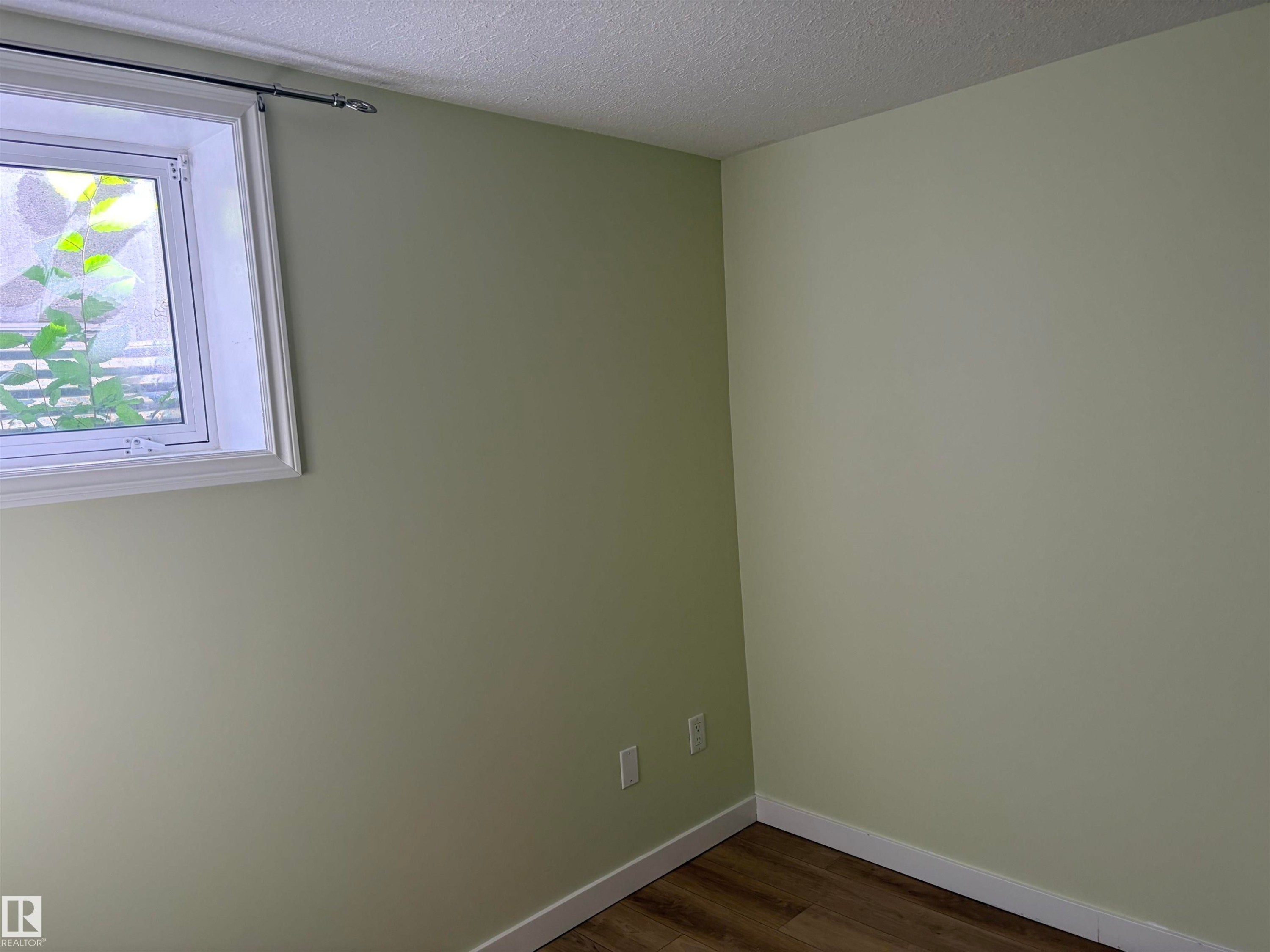 White-trimmed window with privacy glass, light green painted walls, and wood-finish flooring Basement - 13219 107 Street Nw, Edmonton, AB