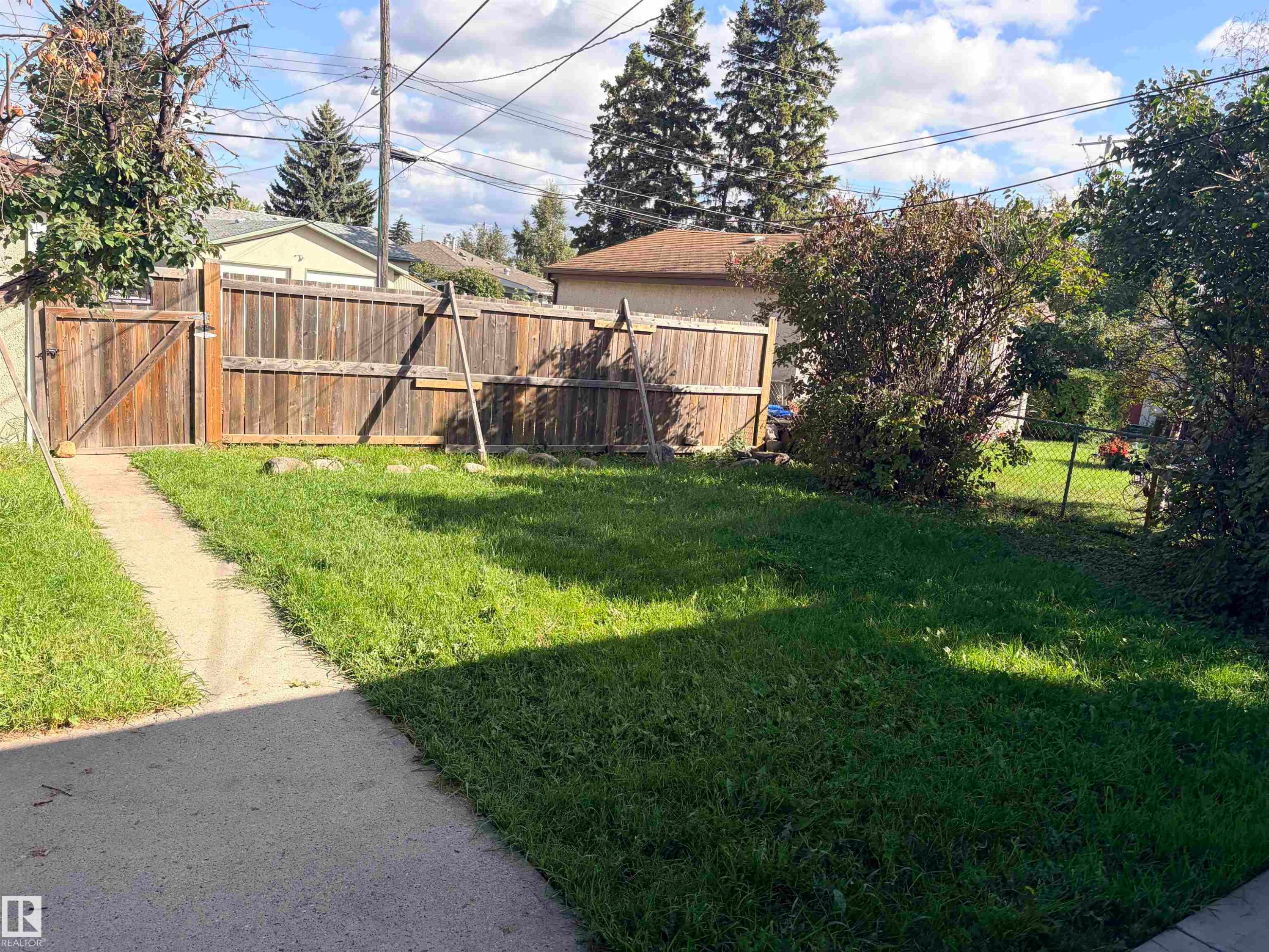 Private fenced backyard with a concrete pathway and mature perimeter landscaping - 13219 107 Street Nw, Edmonton, AB