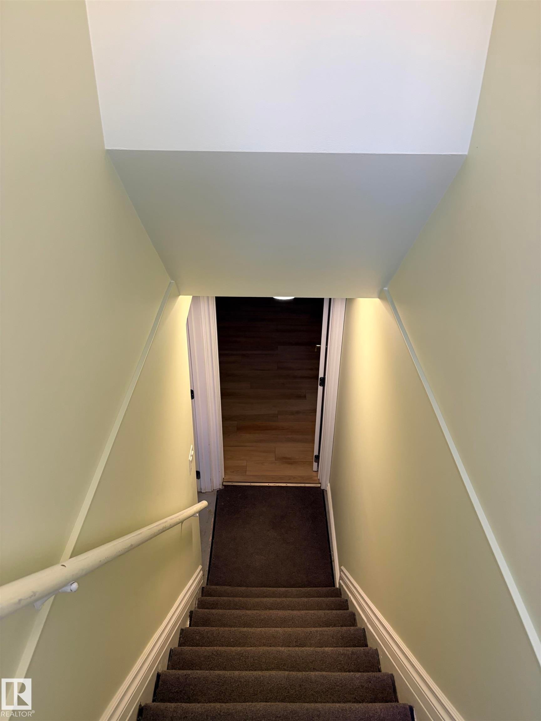 Carpeted staircase with a white handrail, leading to a landing with wood-finish flooring - 13219 107 Street Nw, Edmonton, AB