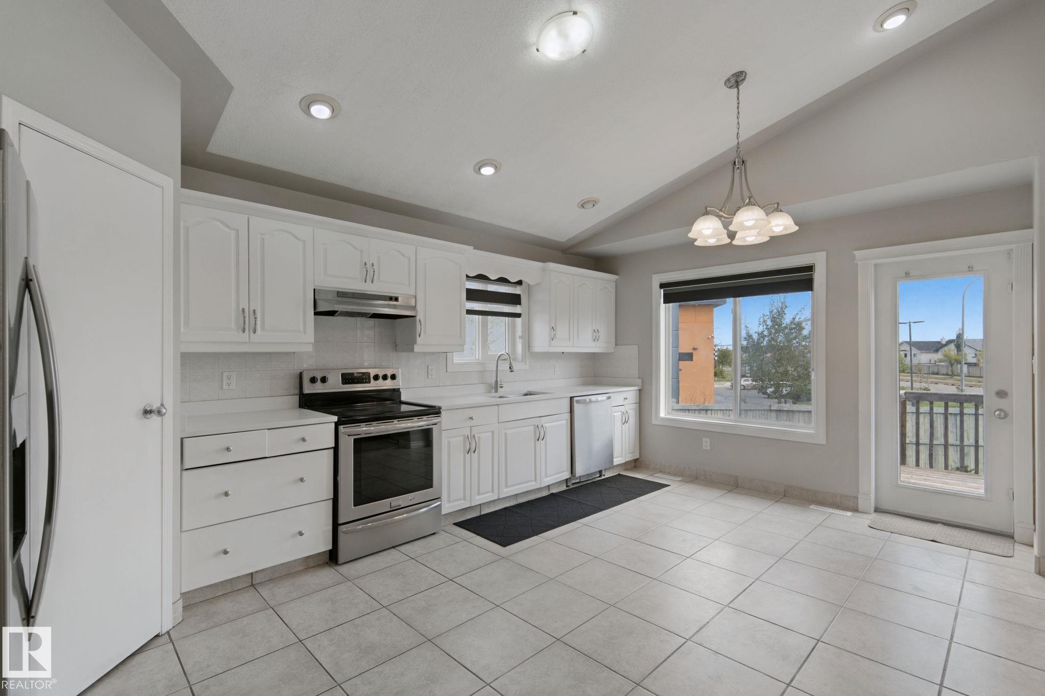 Kitchen featuring white cabinetry, stainless steel appliances, tiled flooring, and a glass-paneled door - 16807 78 Street Nw, Edmonton, AB