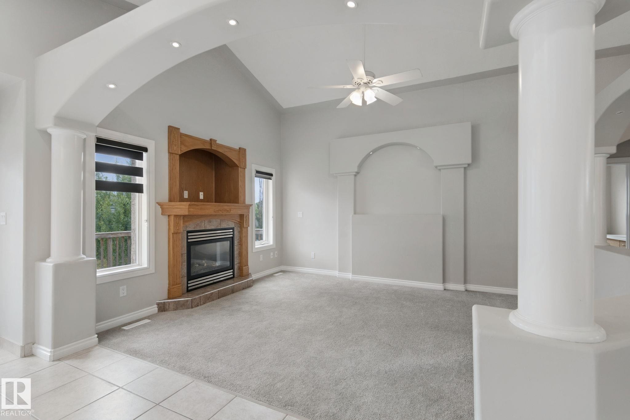 Vaulted ceiling with recessed lighting, central ceiling fan, wood-mantled fireplace with tile surround, large windows with shades, and decorative interior columns - 16807 78 Street Nw, Edmonton, AB