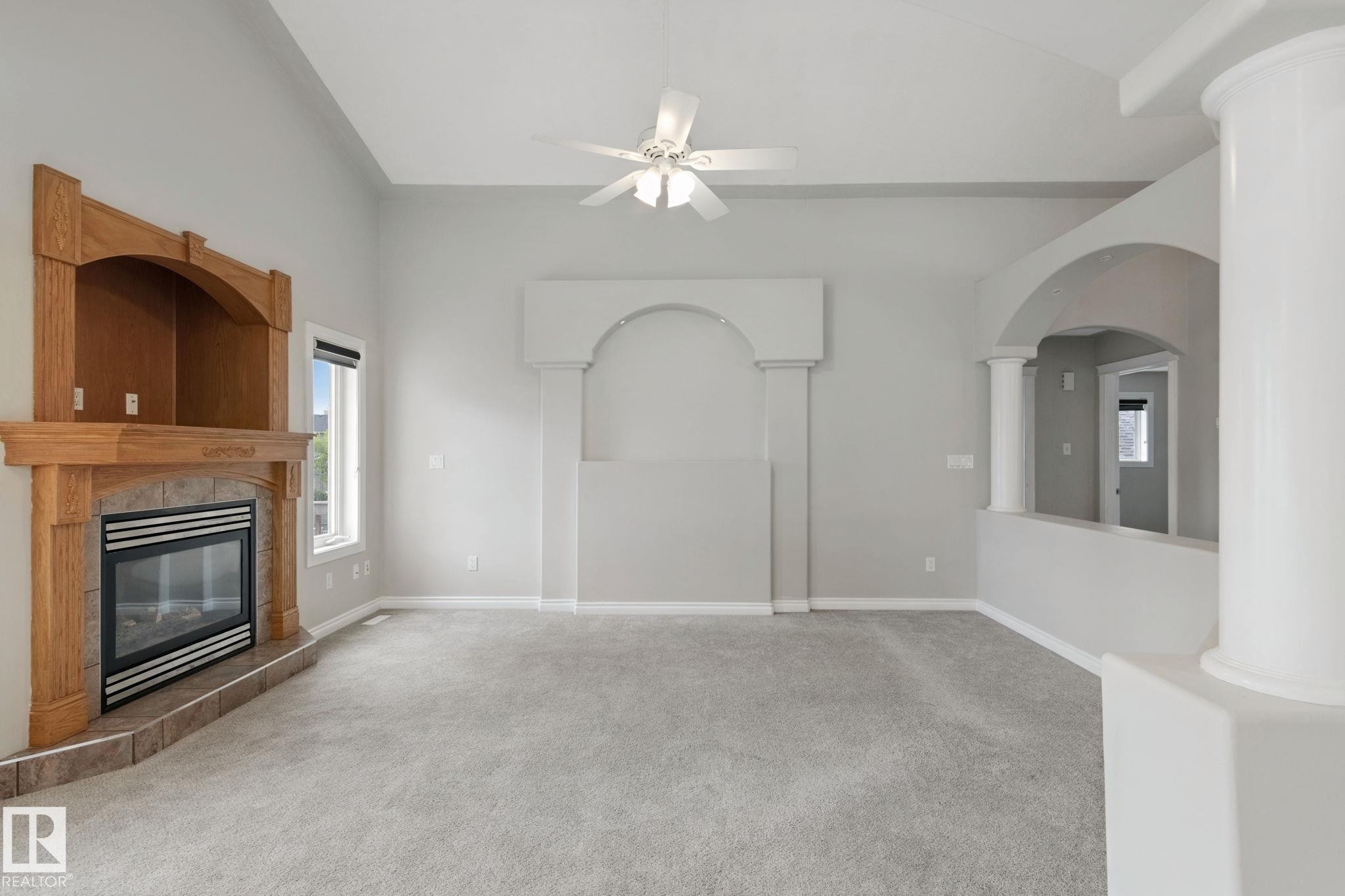 Vaulted ceiling with a ceiling fan, fireplace with a wood mantle, arched architectural features, and light-toned carpeting - 16807 78 Street Nw, Edmonton, AB
