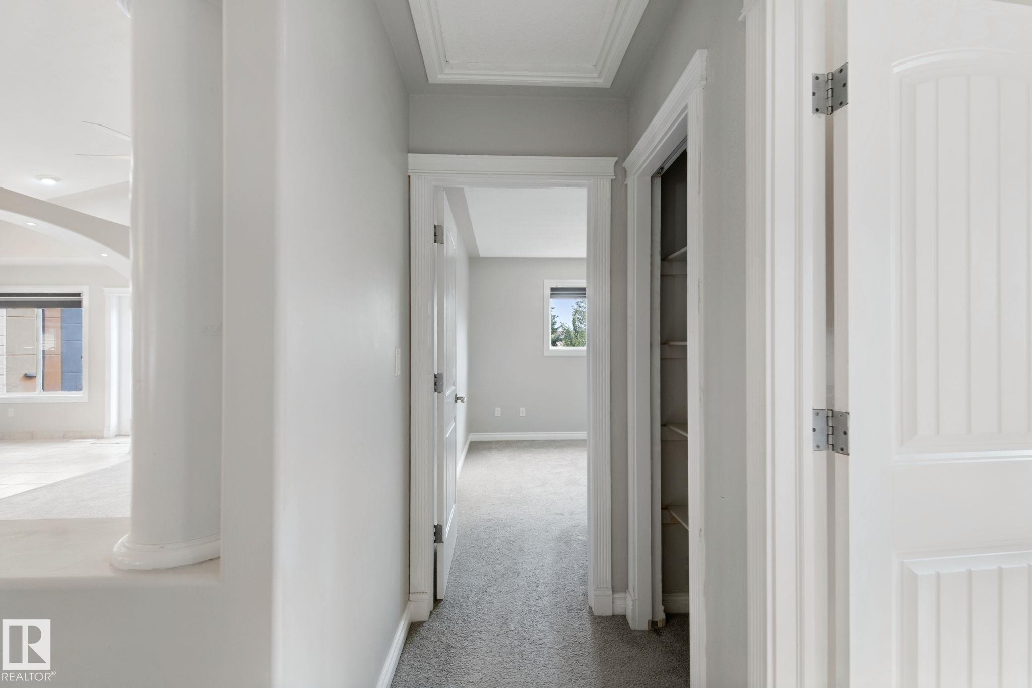 Hallway with carpet flooring, white paneled doors, and a built-in linen closet - 16807 78 Street Nw, Edmonton, AB