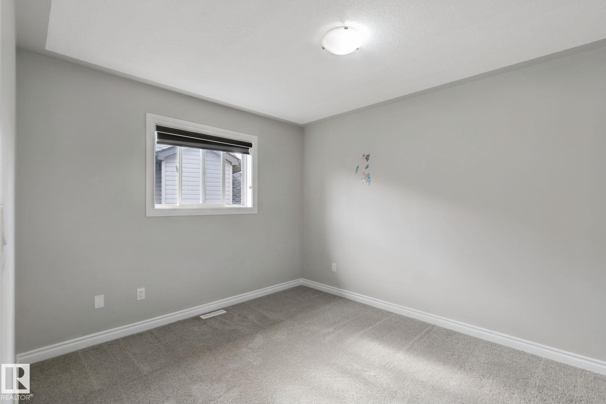 Neutral gray wall paint with white trim, carpeting, a single window with blinds, and an overhead flush-mount light fixture - 16807 78 Street Nw, Edmonton, AB