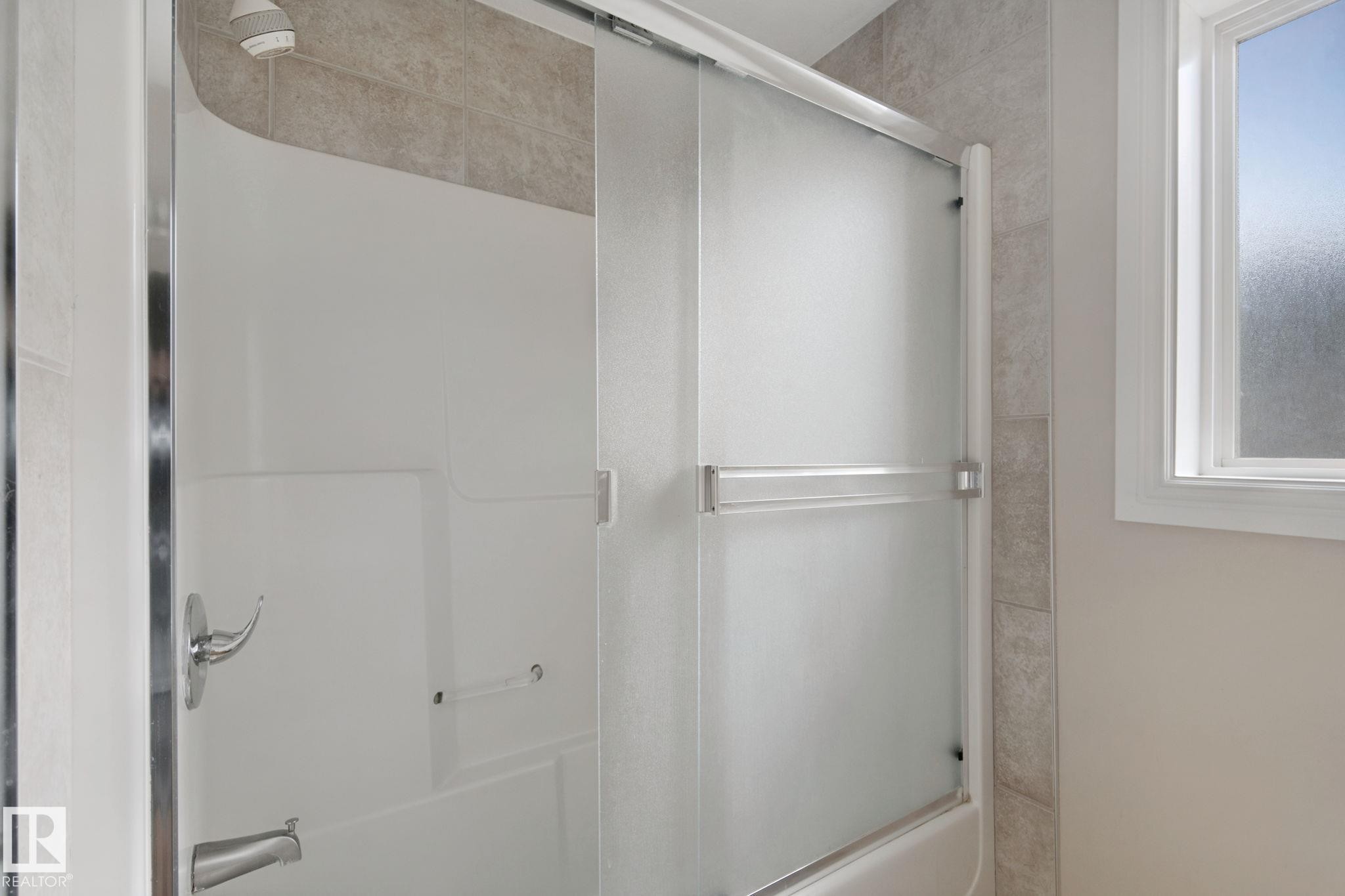 Tub/shower combination with chrome fixtures, sliding frosted glass doors, and tiled surround - 16807 78 Street Nw, Edmonton, AB