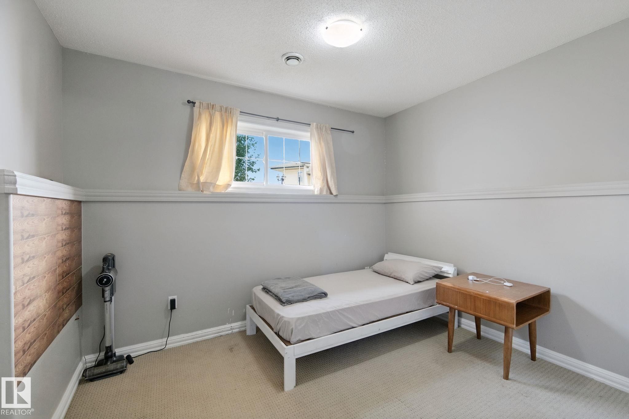 Carpeted room with light gray walls, a window with exterior visibility, a wall-mounted light fixture, and crown molding - 16807 78 Street Nw, Edmonton, AB