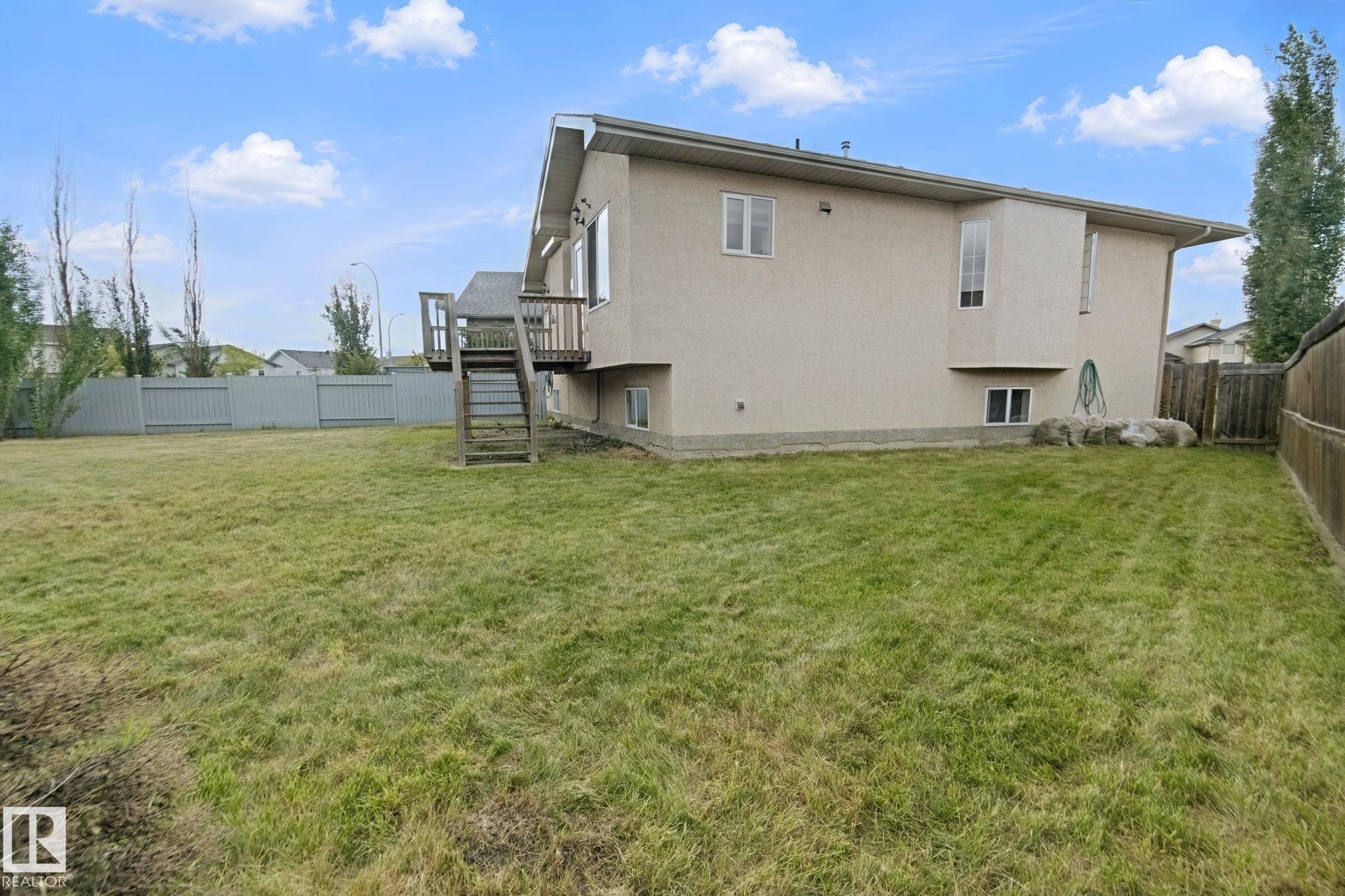 Expansive grassy yard featuring a wood deck with stairs, a privacy fence, and multiple windows - 16807 78 Street Nw, Edmonton, AB