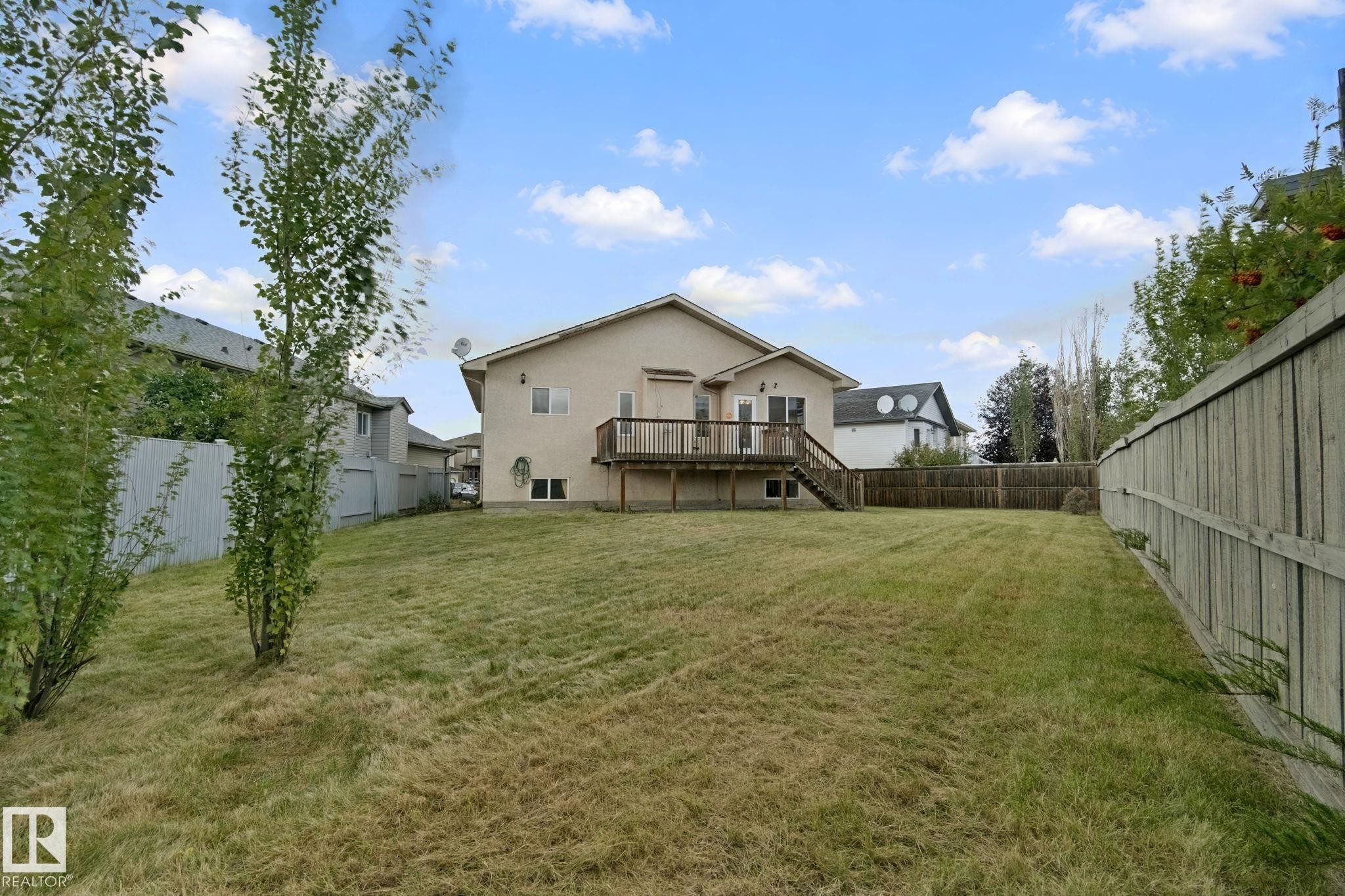 Expansive backyard featuring a wood privacy fence, a multi-level wood deck, and a stucco exterior with multiple windows - 16807 78 Street Nw, Edmonton, AB