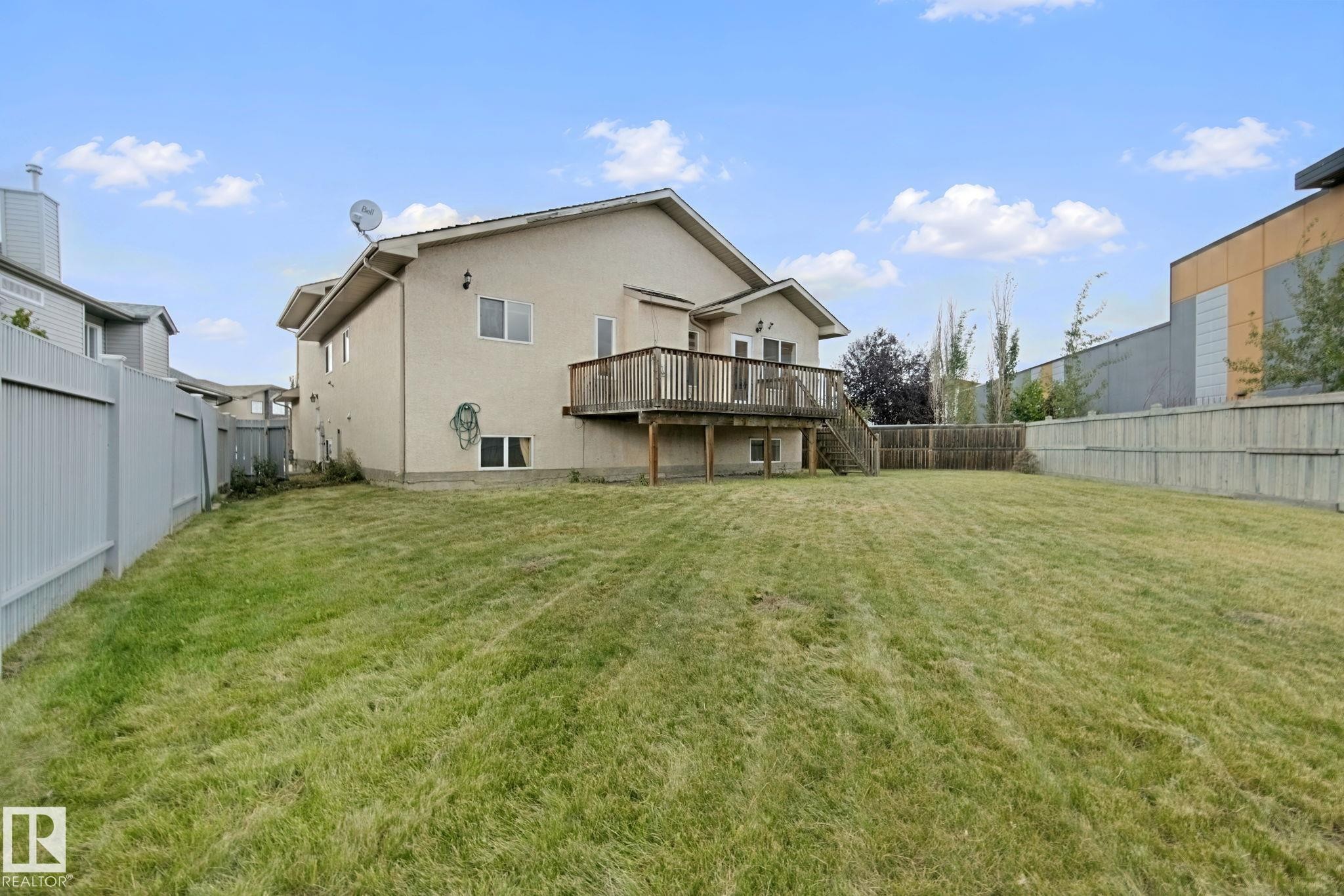 Spacious backyard featuring a wooden deck, mature trees, and privacy fencing - 16807 78 Street Nw, Edmonton, AB