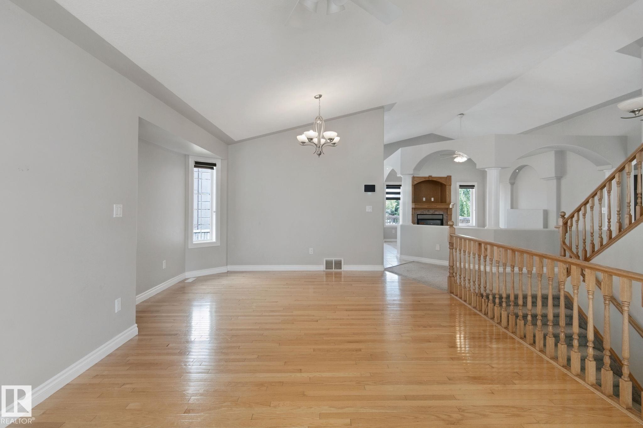 Vaulted ceilings, wood-finish flooring, staircase with wood railing, recessed fireplace with built-in shelving, and arched architectural details - 16807 78 Street Nw, Edmonton, AB